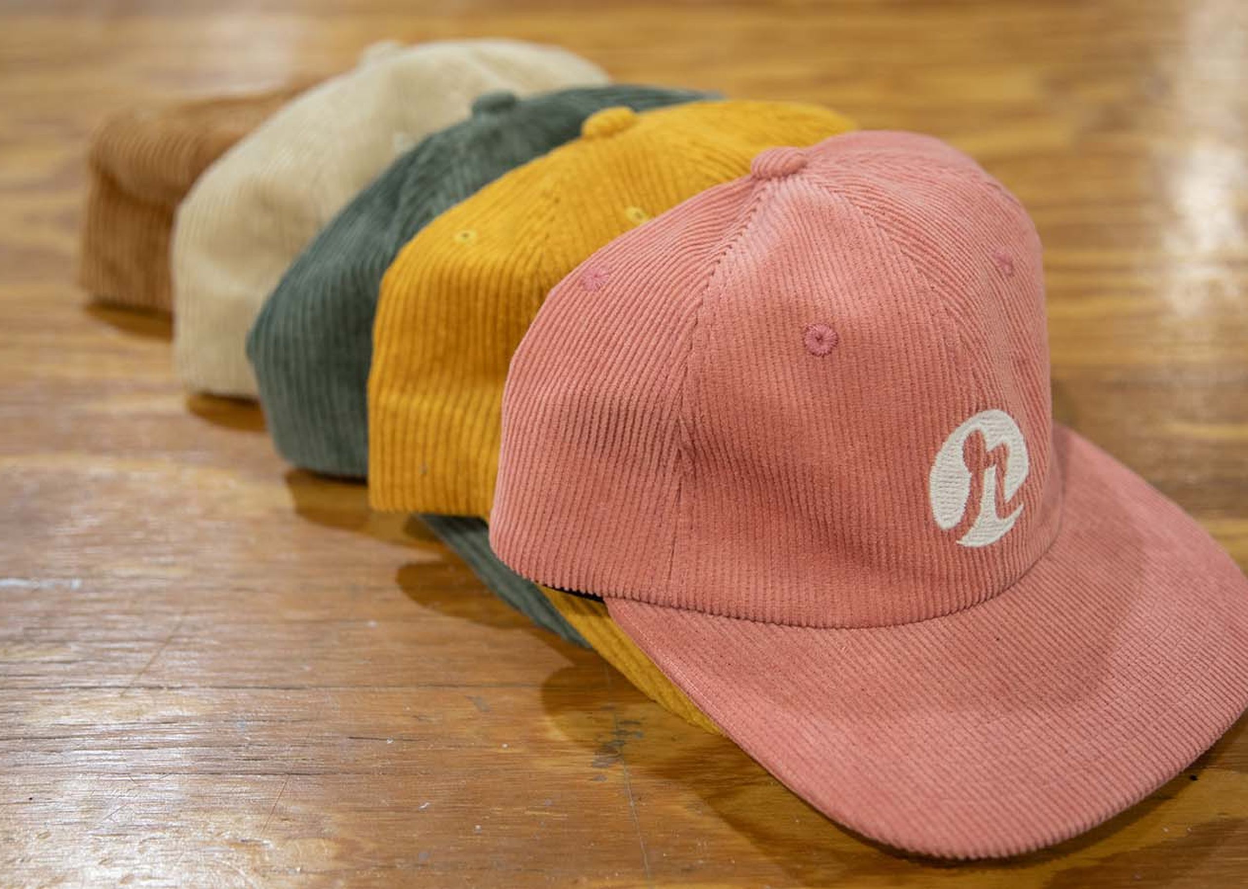 A stack of hats on a wood table. Brown, white, dark green, yellow, and pink from back to front