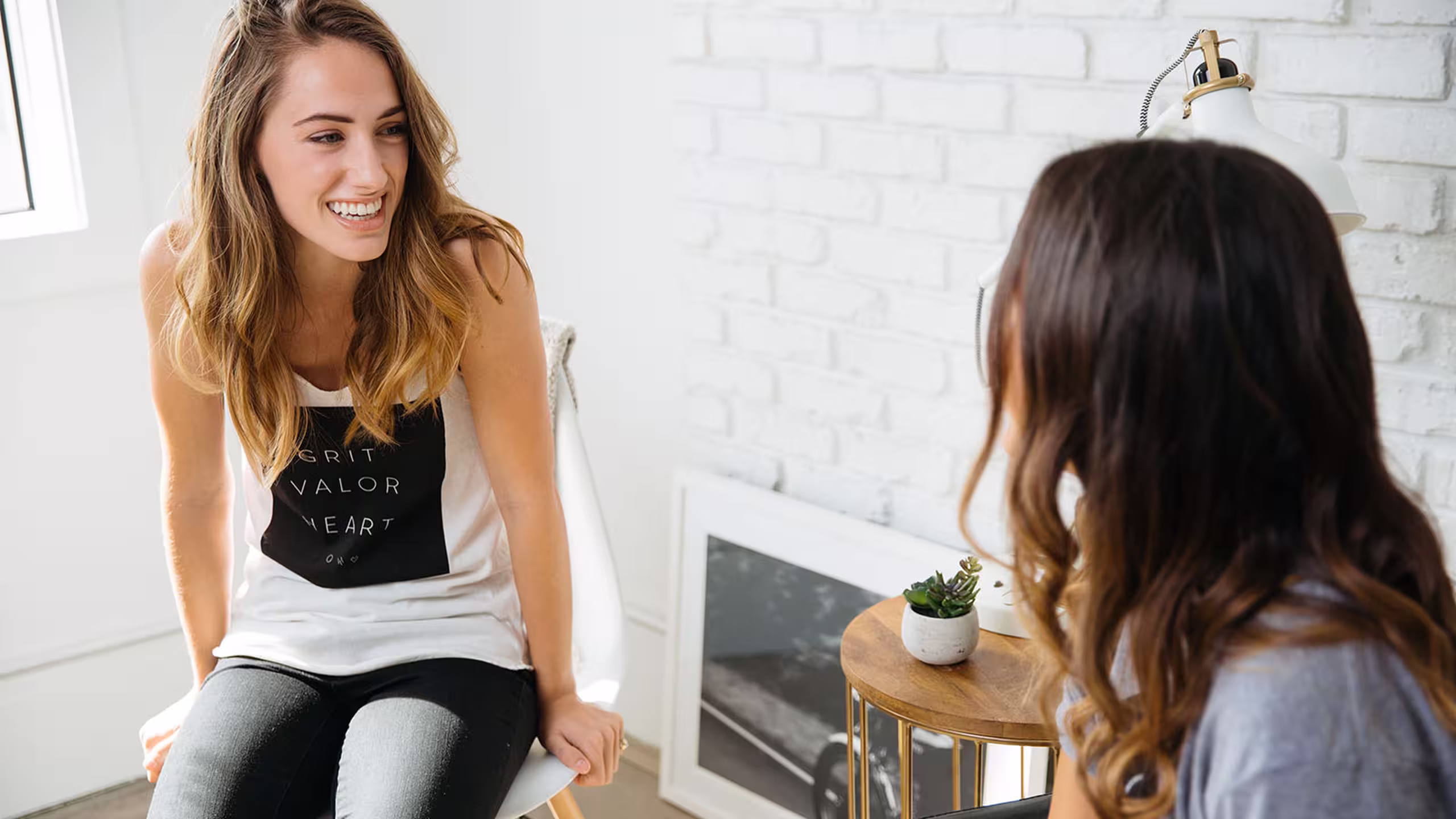 two women talking to each other, one wearing a white tank top