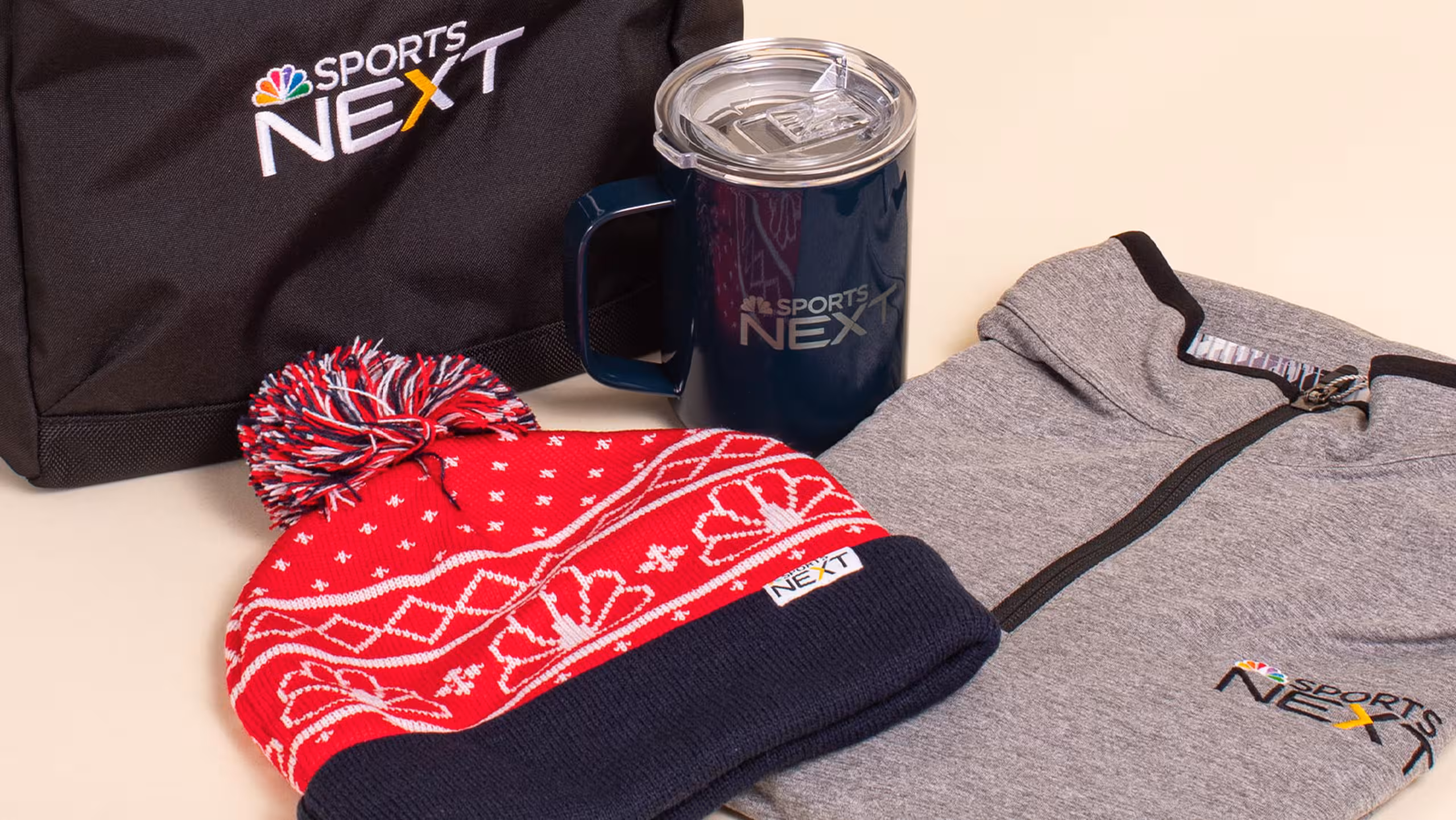 a collection of items—winter hat, travel coffee mug, zip-up shirt, and a embroidered bag