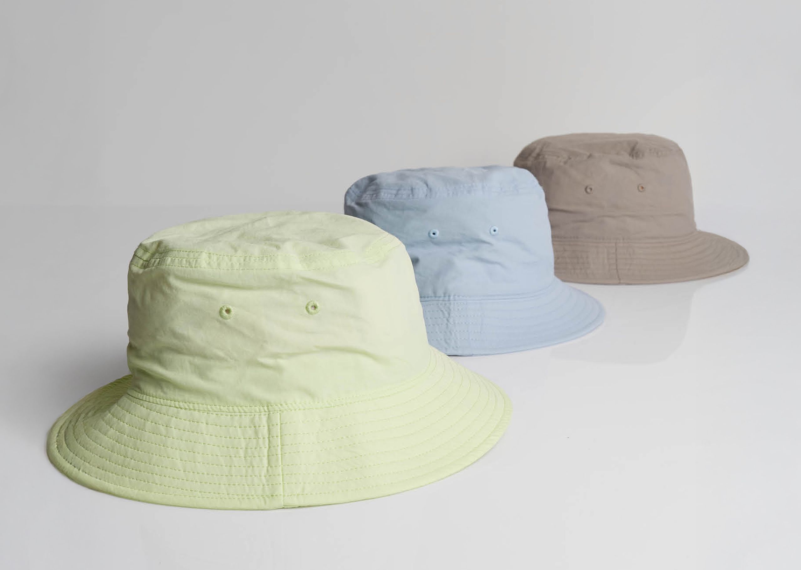three bucket hats, lime, powder blue, and mushroom brown, on a white background