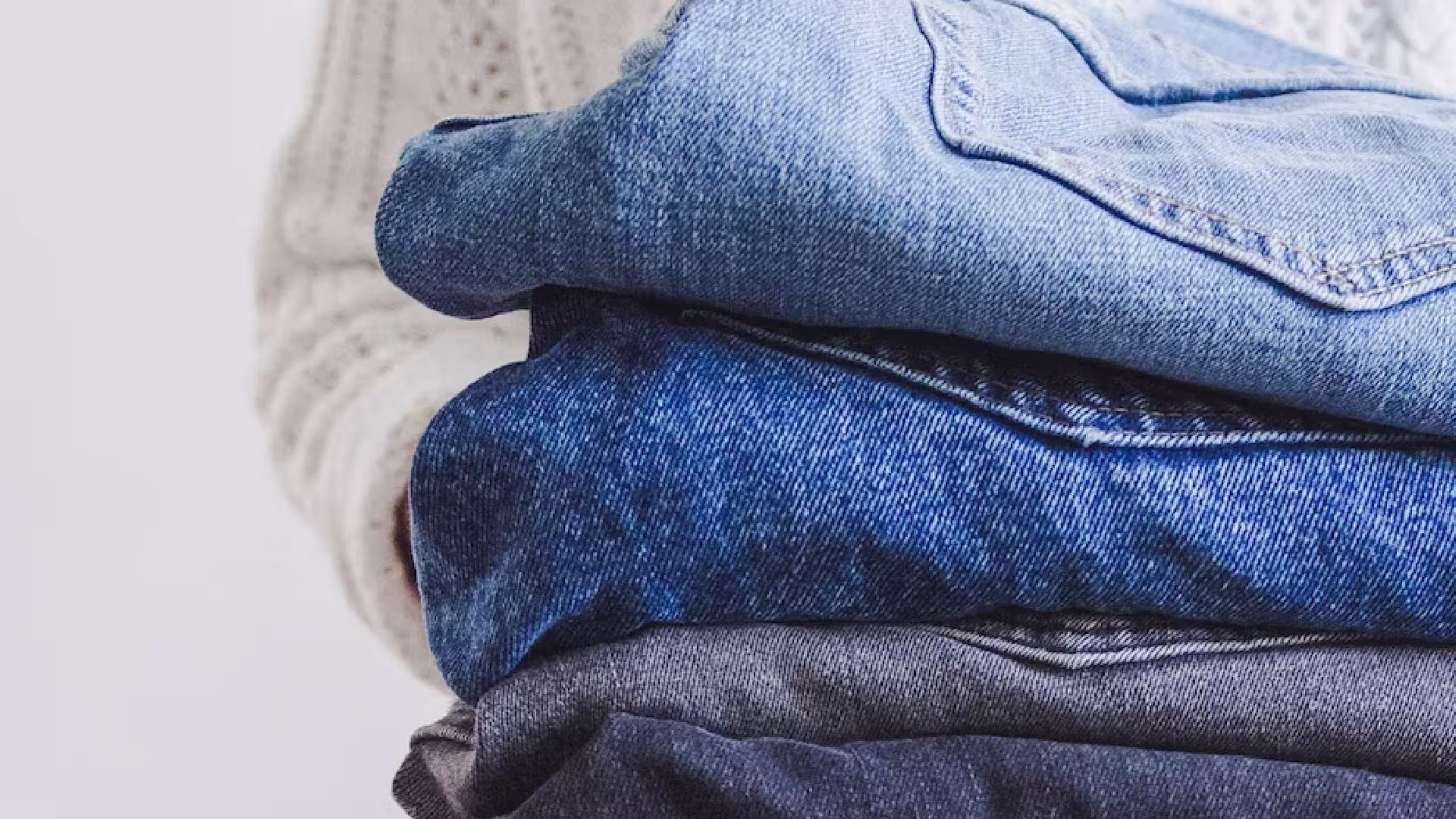 A person holding a stack of jeans