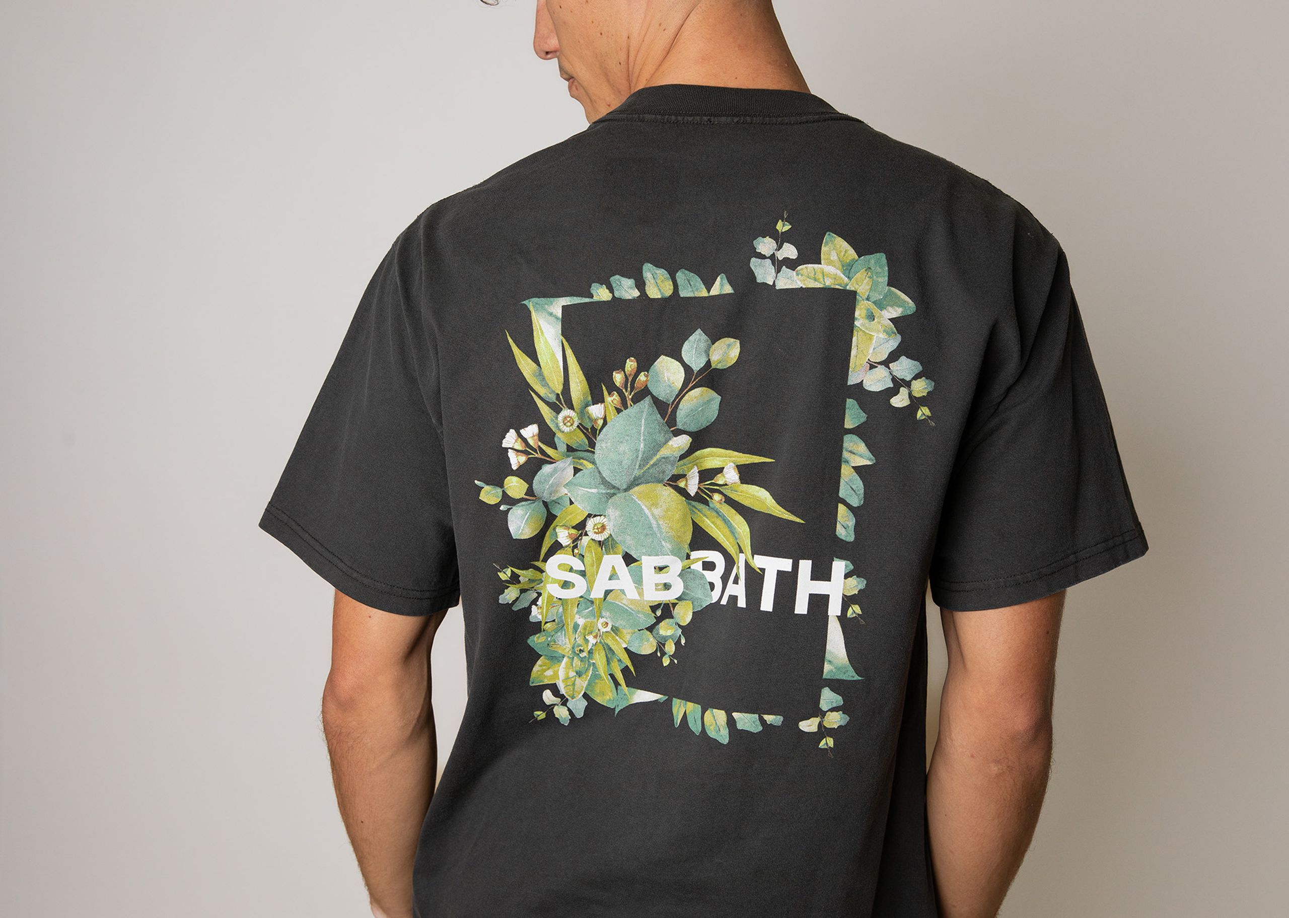 the back of a man wearing a black t-shirt with leaves and the word sabbath screen printed