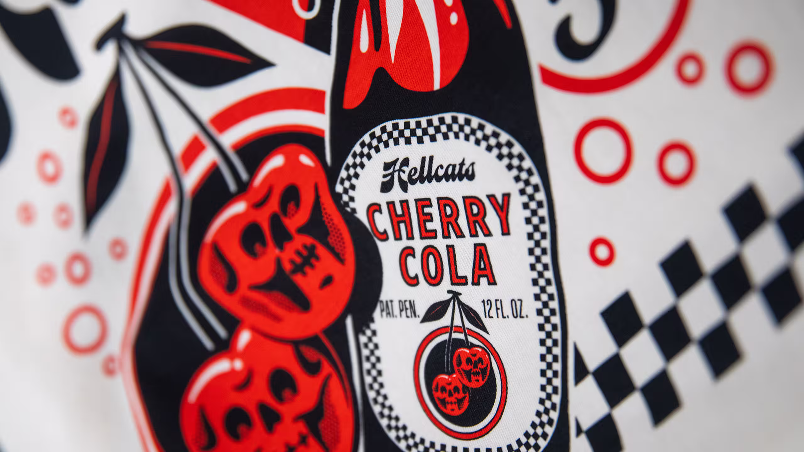 close up of a hellcats design of a cherry cola bottal on a white tee