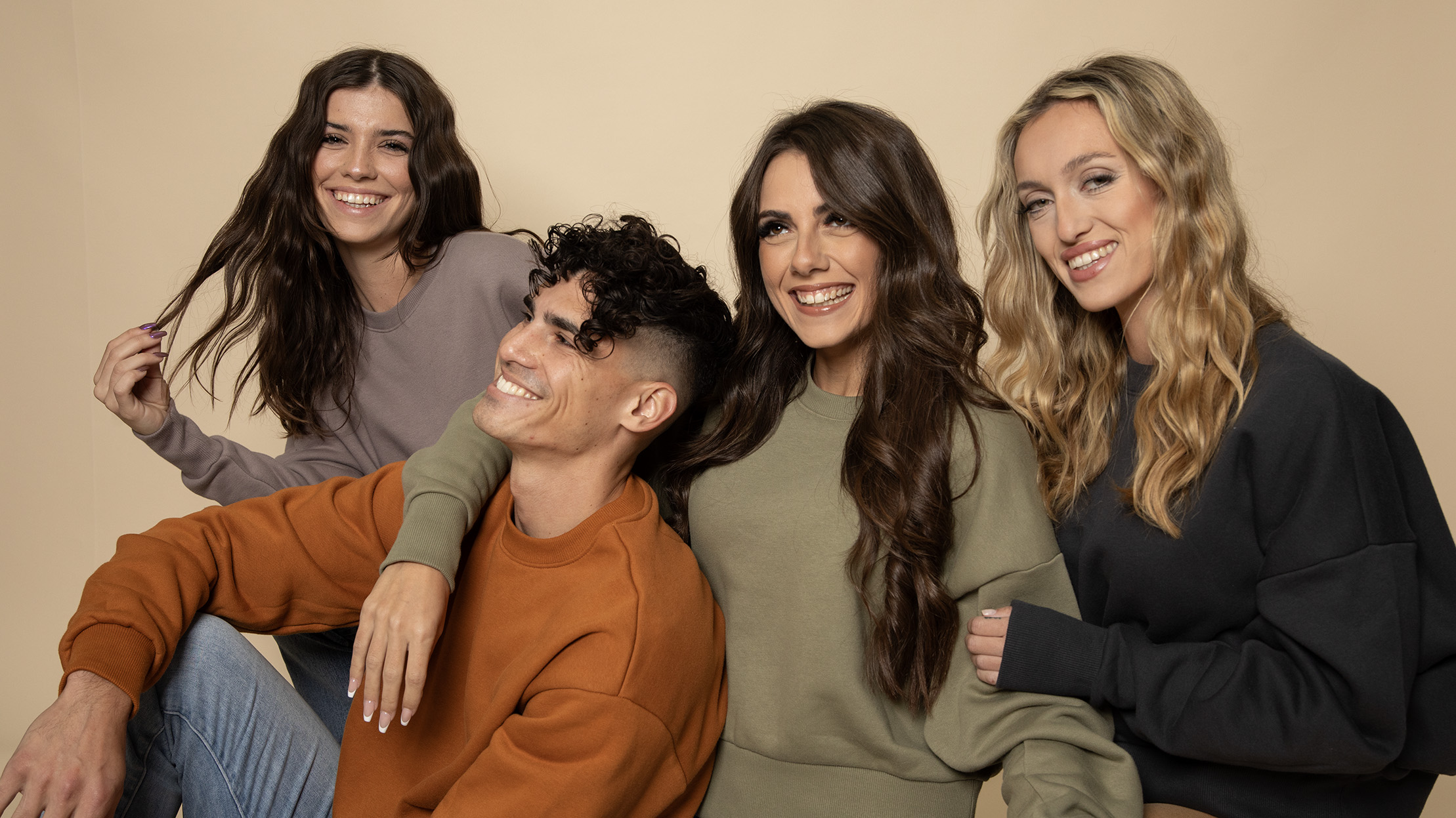 Four people smiling, wearing casual sweaters in earthy tones, pose against a beige background.