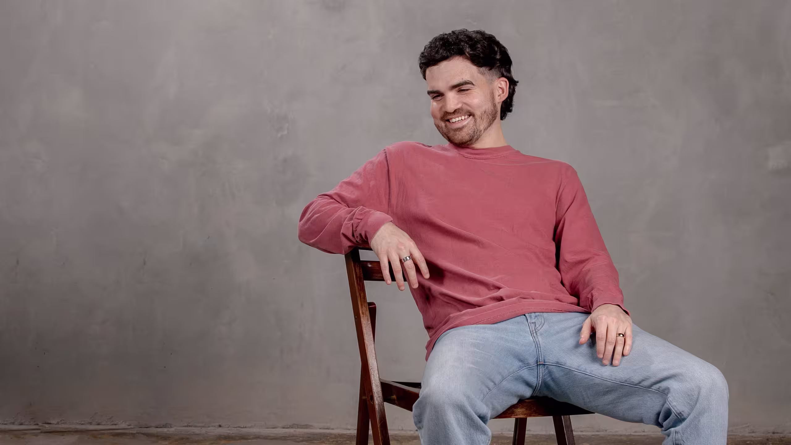 man wearing a red long sleeve t-shirt while sitting in a wooden chair