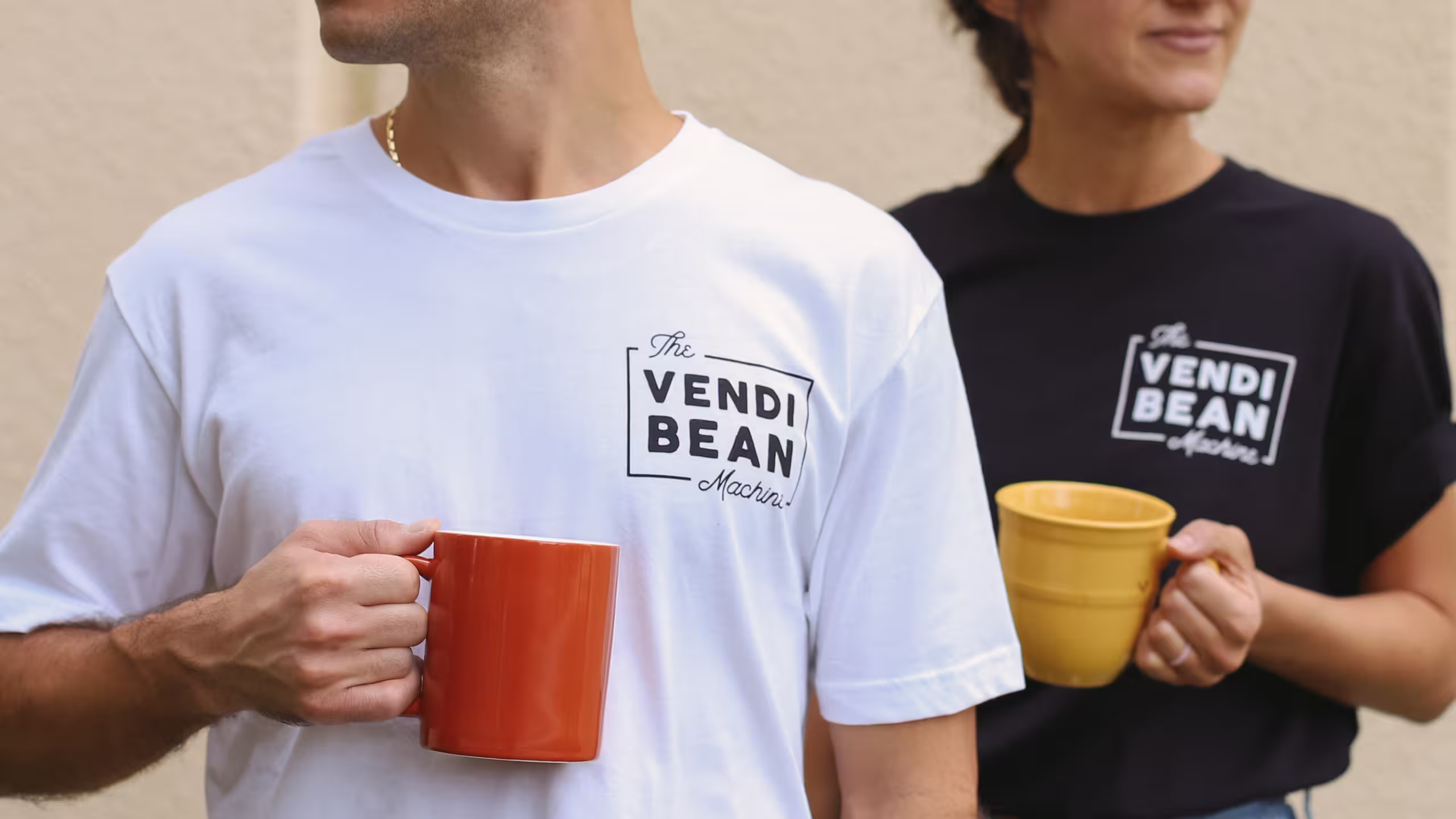 a man and women holding coffee cups with vendi bean t-shirts