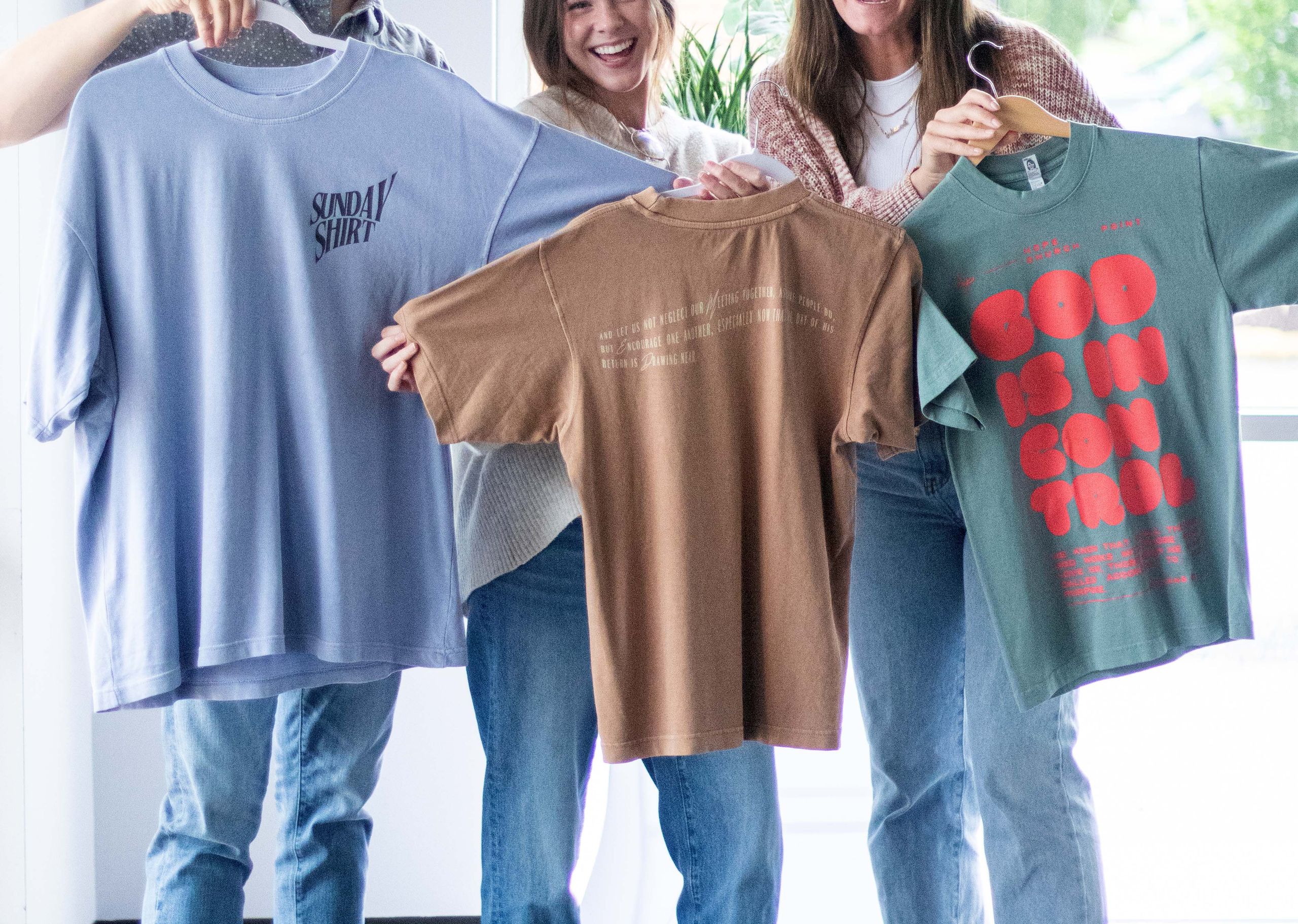 three people holding three different color boxy t-shirts