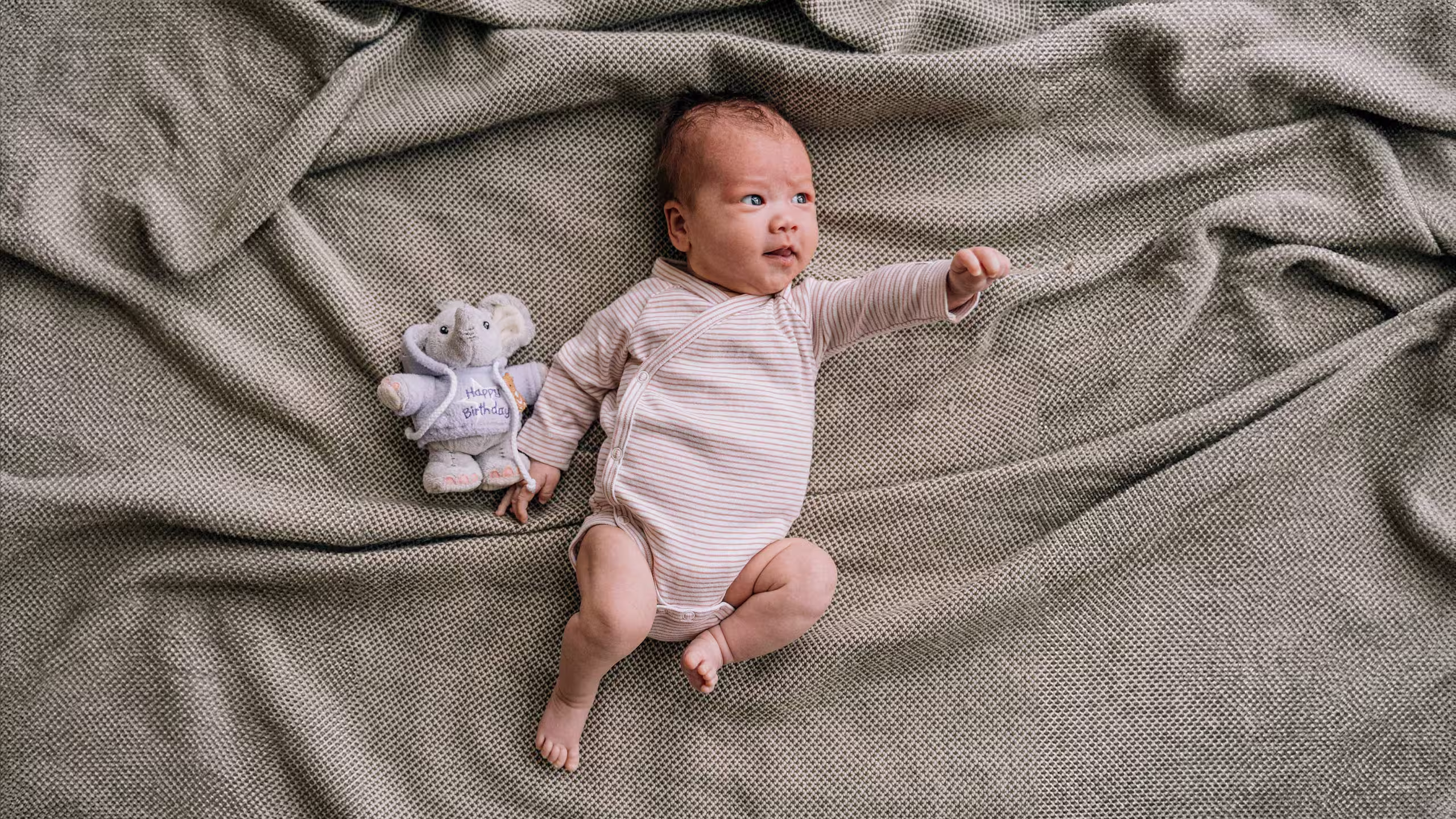 baby in a onesies laying on a gray blanket