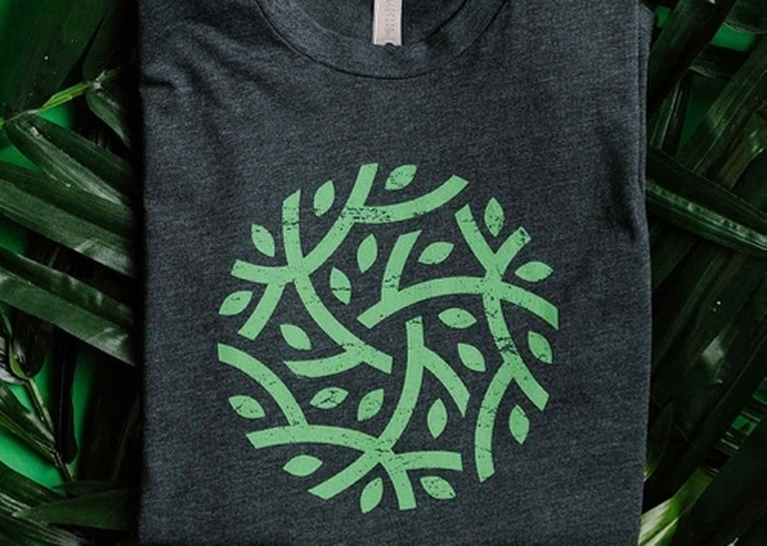 Green branch and leaf design inside of circle printed on a dark green shirt