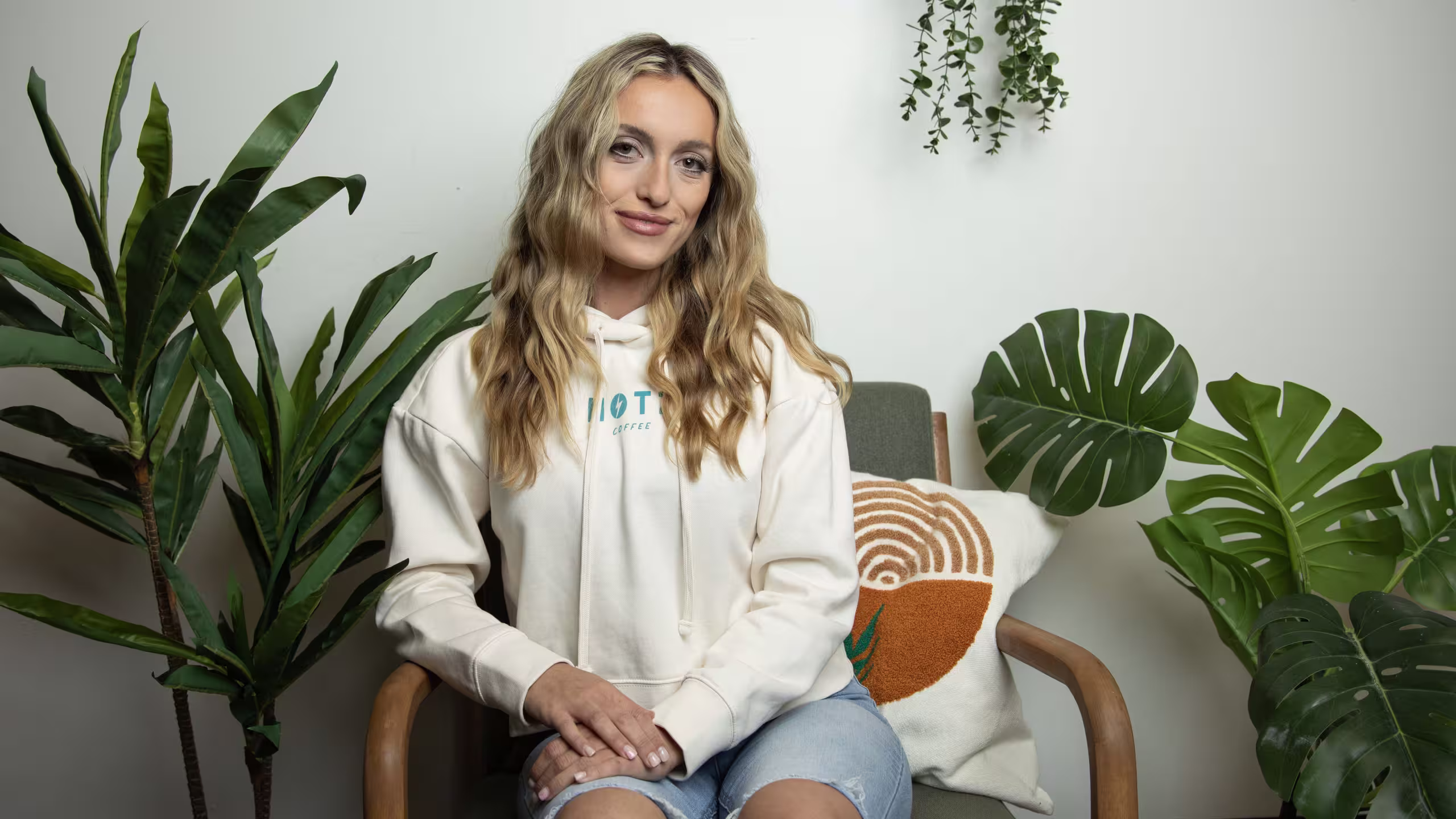 Women sitting wearing a white hoodie with blue wordmark printed on it