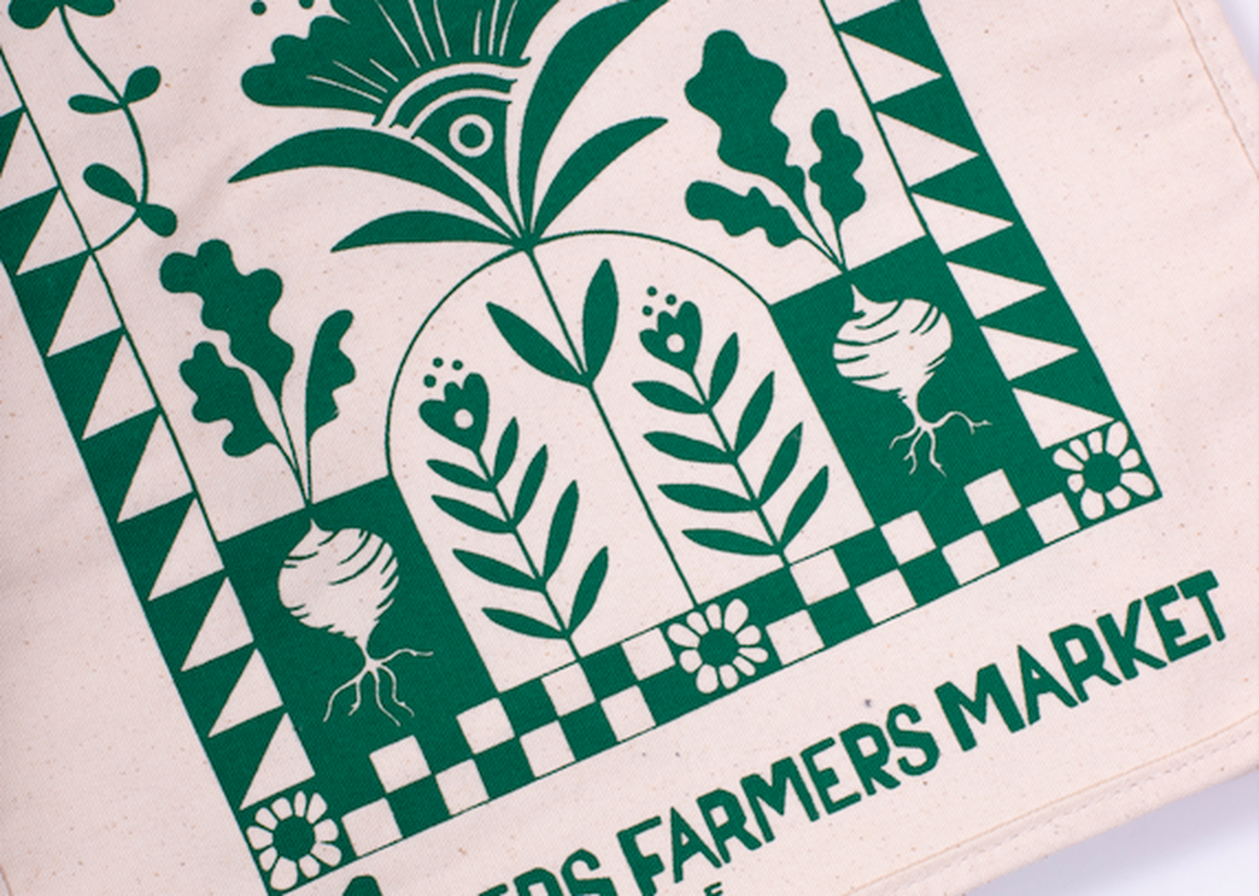 a tote bag printed with green ink with an earthy design and text that says "Sisters Farmers Market"