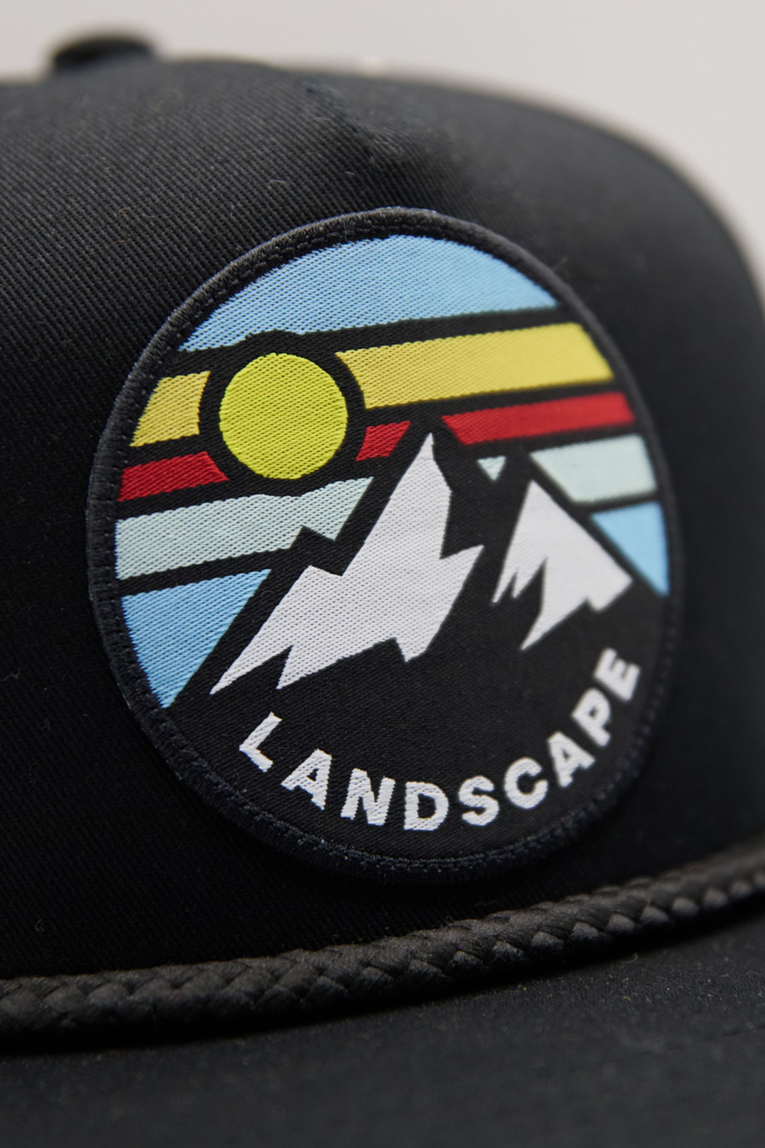close up a woven patch of a mountain and sun illustration on a black hat