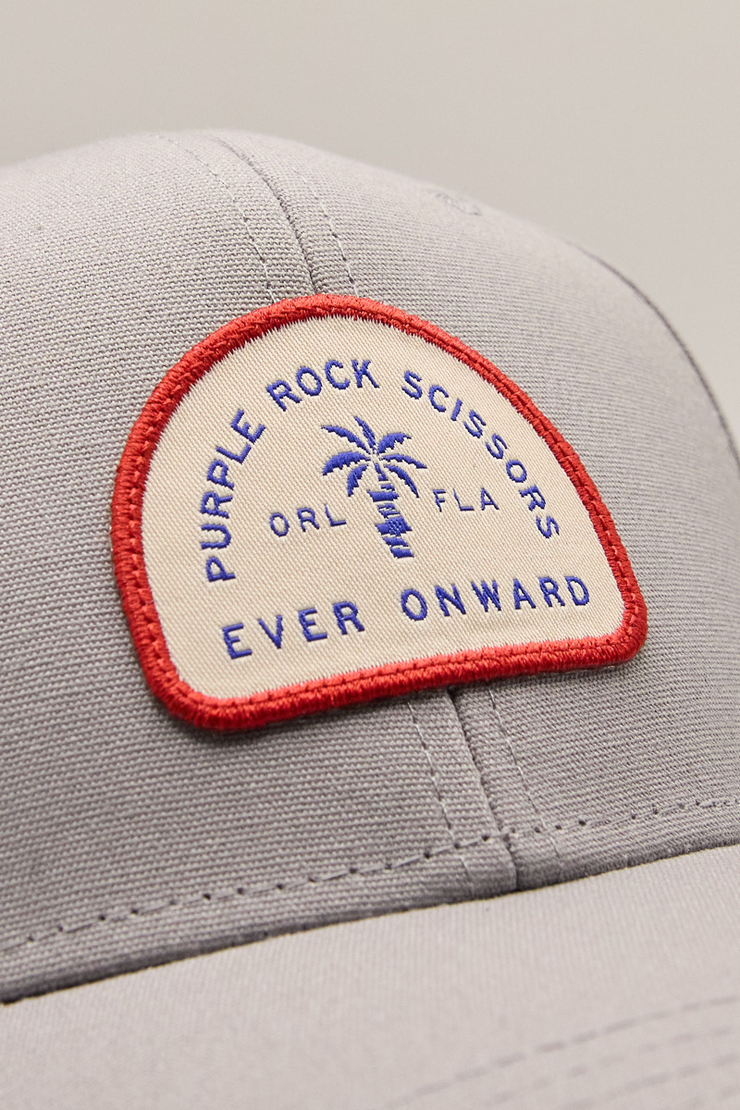 close up of a white and red woven patch with the words purple rock scissors - ever onward and a palm tree illustration