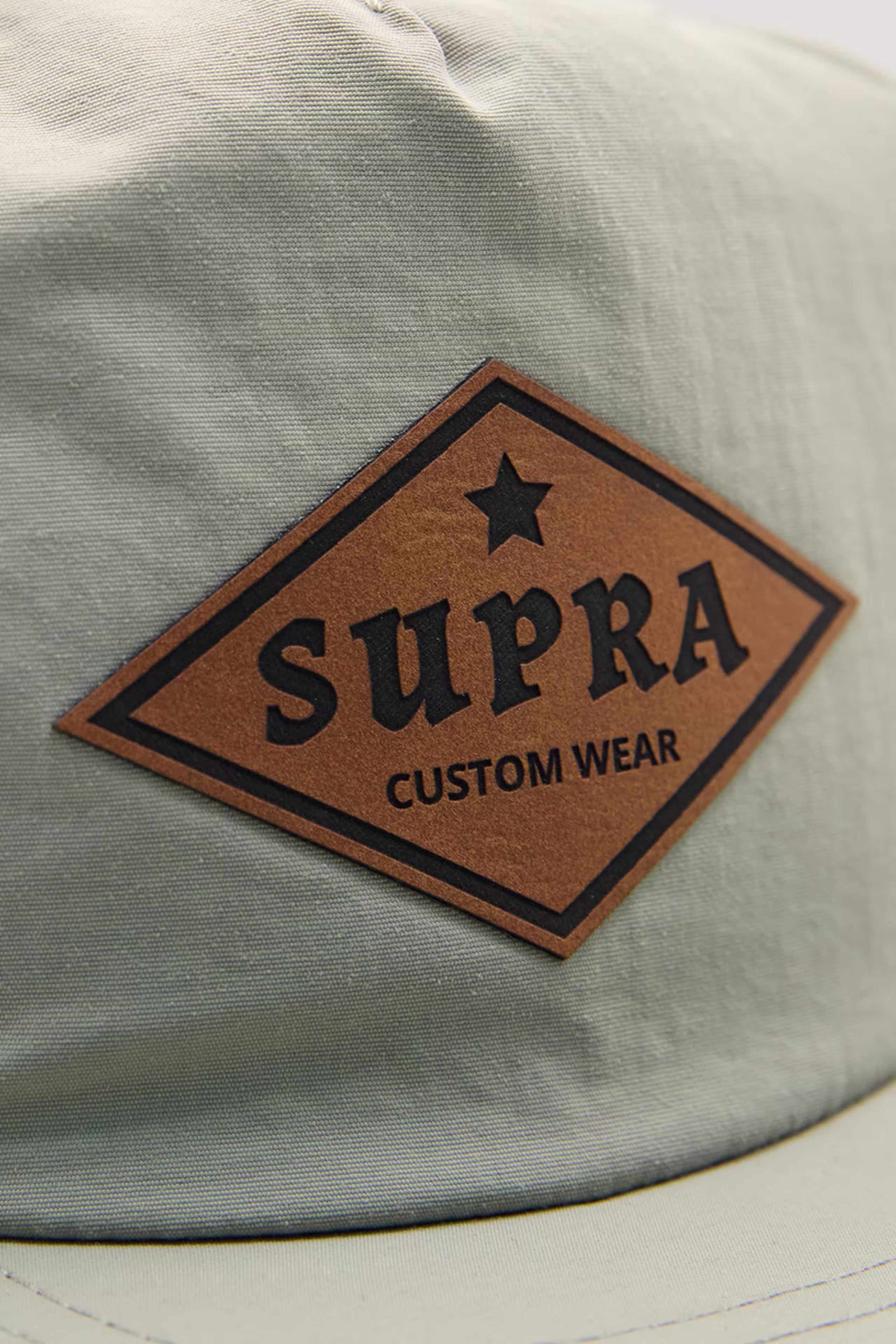 a diamond-shaped faux leather patch on a sage green hat