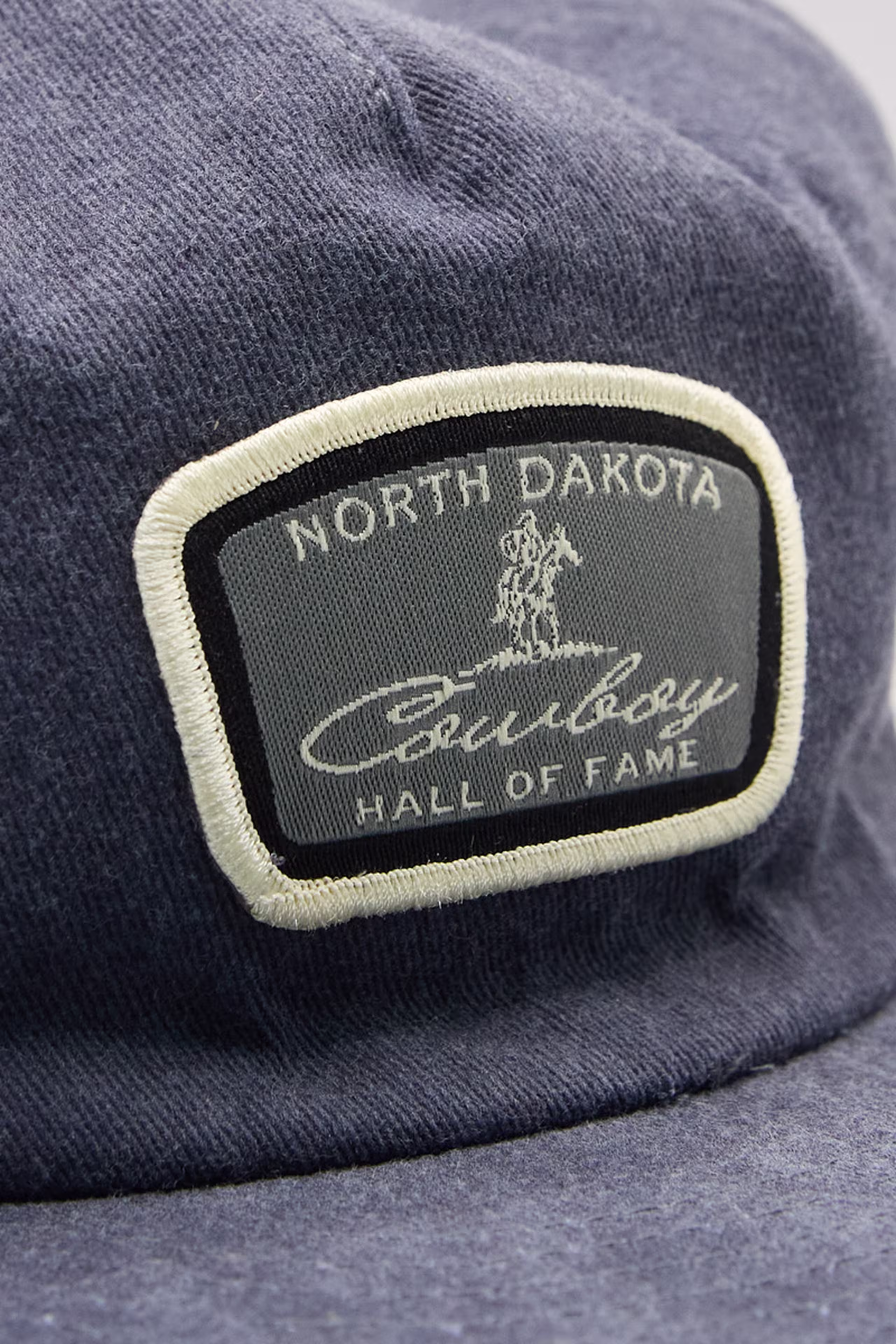 a woven patch that is blue, navy, and white on a dark blue denim hat