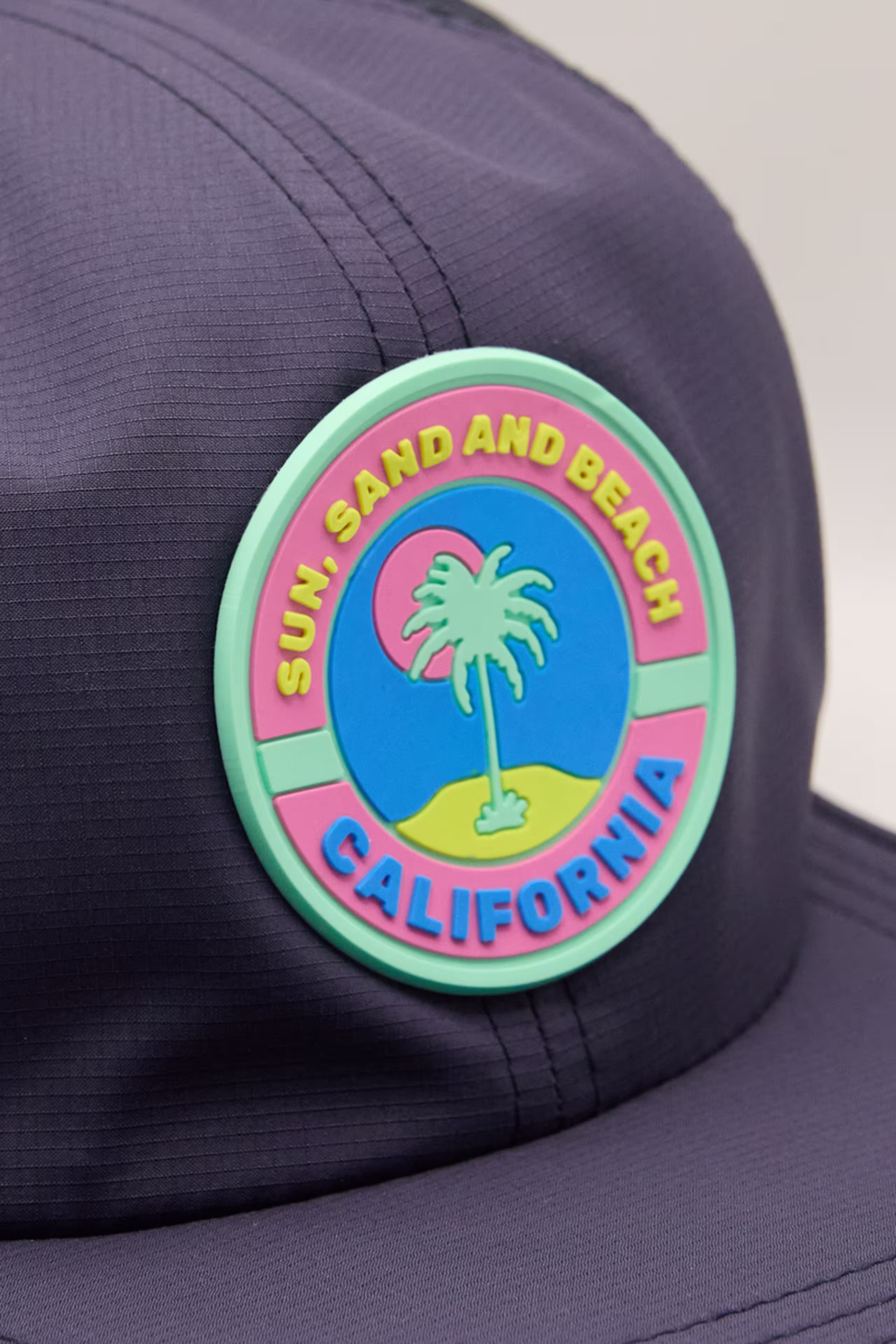 a neon colored palm tree and sun circle molded patch on a navy hat