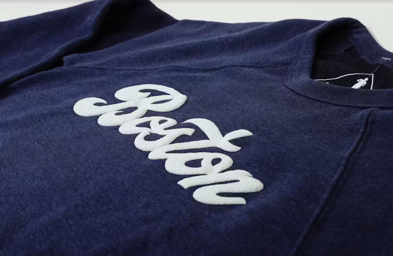 a white word "boston" printed in puff print on a navy t-shirt in a script font