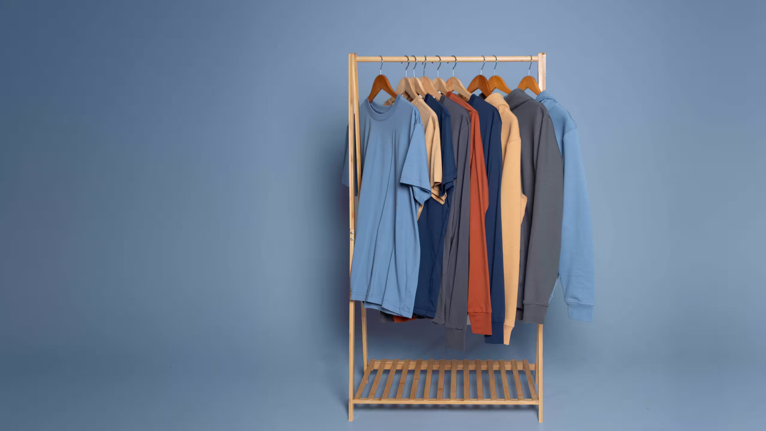 hoodies and t-shirts on a wooden rack in front of a blue background