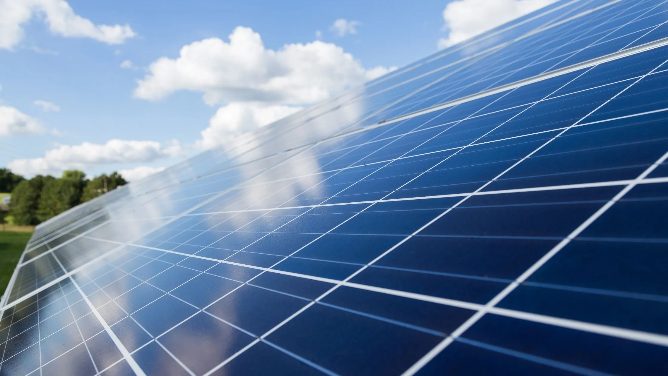 Close-up of solar panels under a blue sky with scattered clouds, reflecting the sky and sunlight.