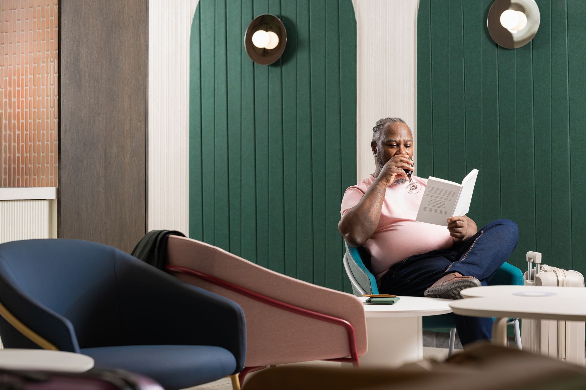 Man sitting in an Escape Lounge with a glass of wine reading a book