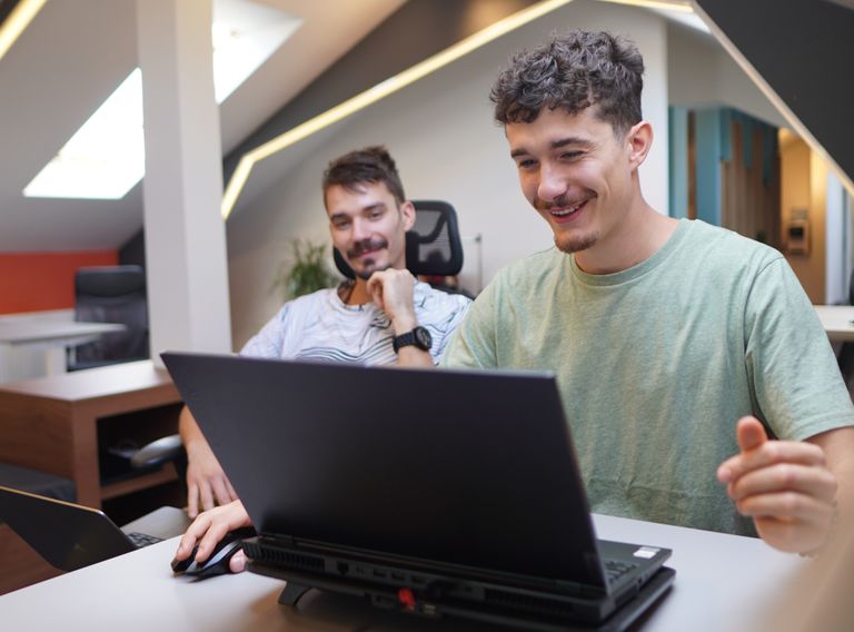 O imagine cu doi studenti la baza7, unul cu laptopul deschis si altul cu un caiet in mana