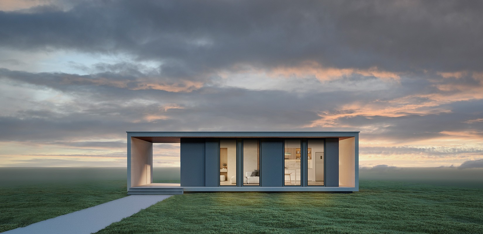 A modern, compact house with large windows and a flat roof, situated in a grassy field under a cloudy sky at sunset.