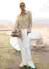 Frau am Strand mit Hahnentritt-Blazer, weißer Hose und Beuteltasche.