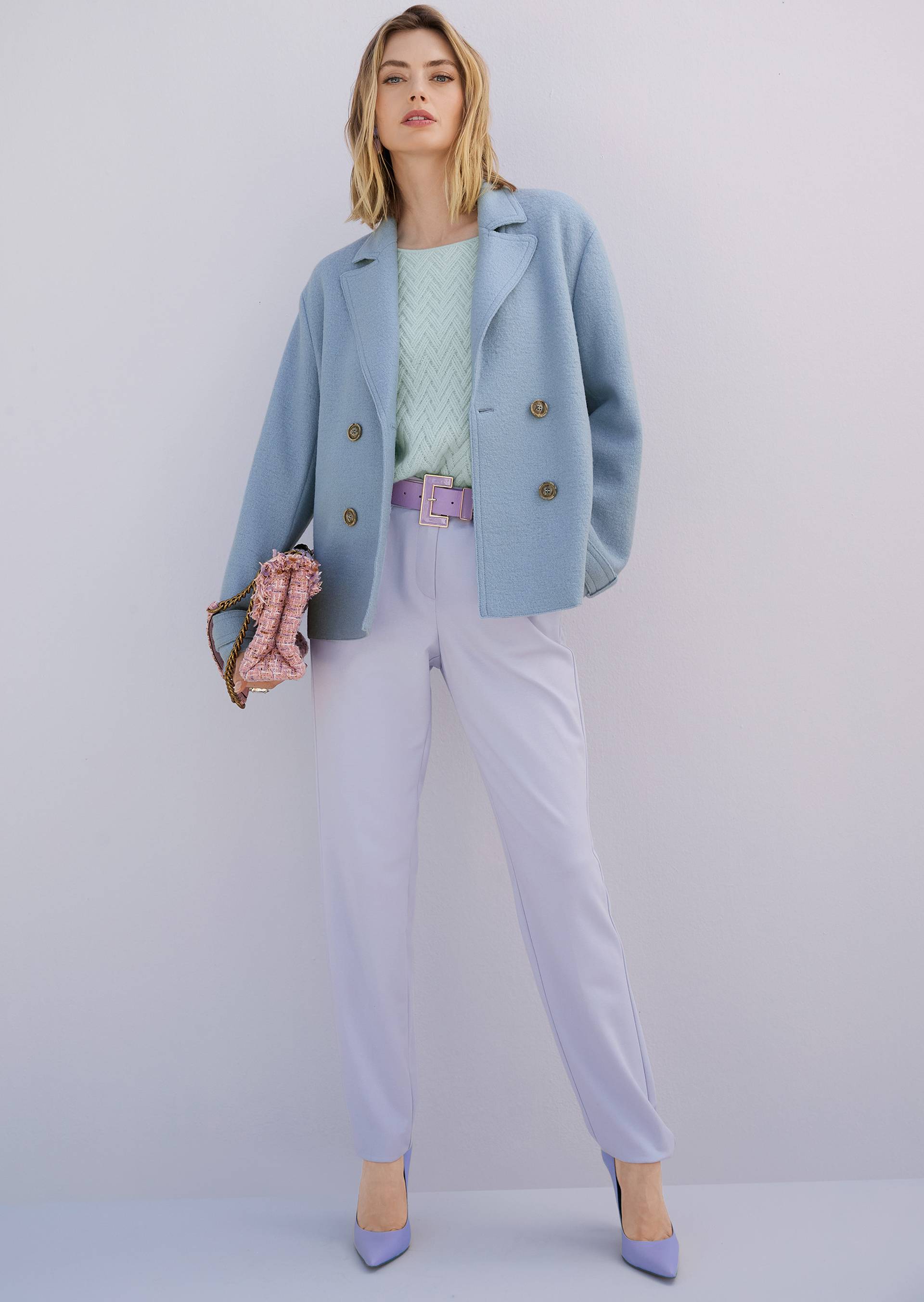 Frau im pastelligen Herbstlook mit hellblauem Blazer, mintfarbenem Pullover und fliederfarbener Hose.