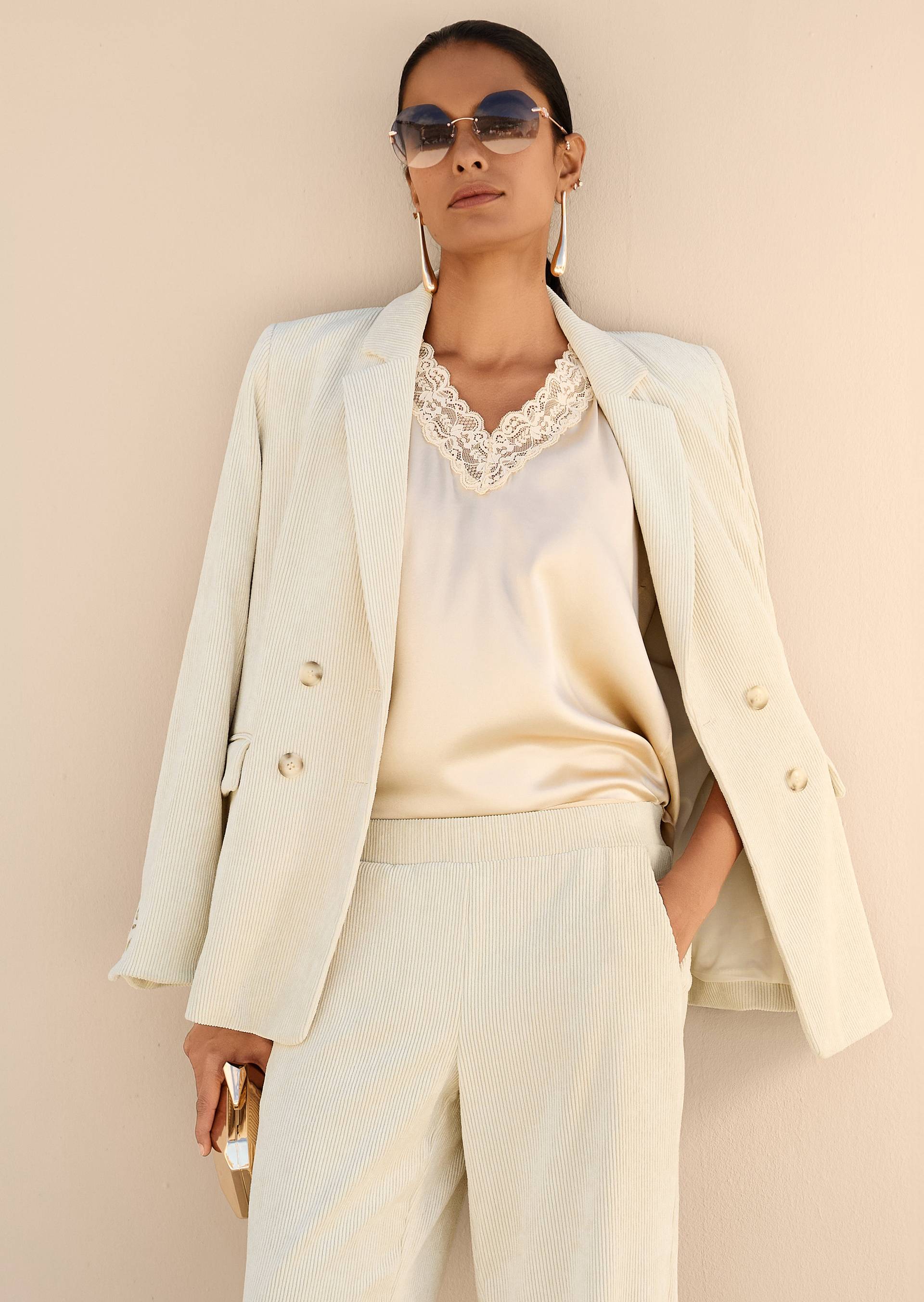 Woman wearing a light-coloured white corduroy suit and a satin top with lace