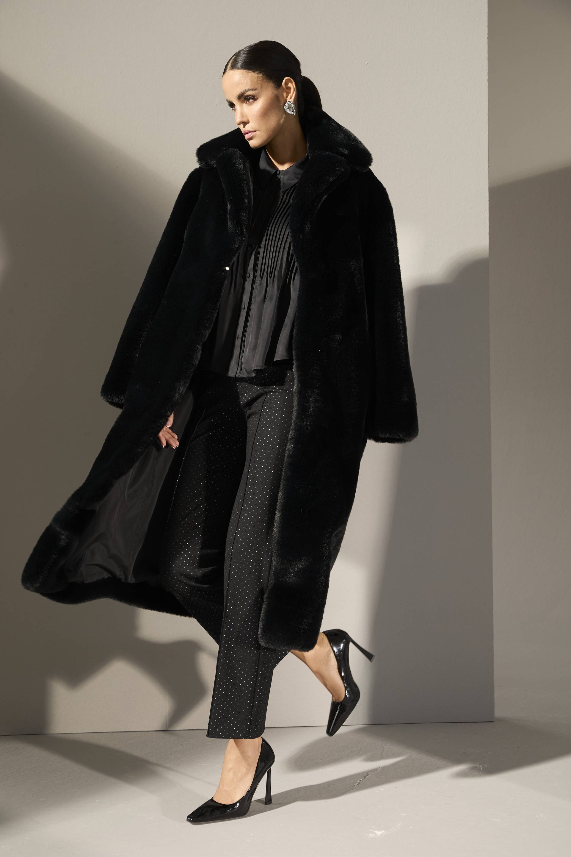 Eine Frau trägt einen langen schwarzen Webpelzmantel in weicher Qualität. 