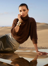 Woman in a brown jumper sitting in front of dunes