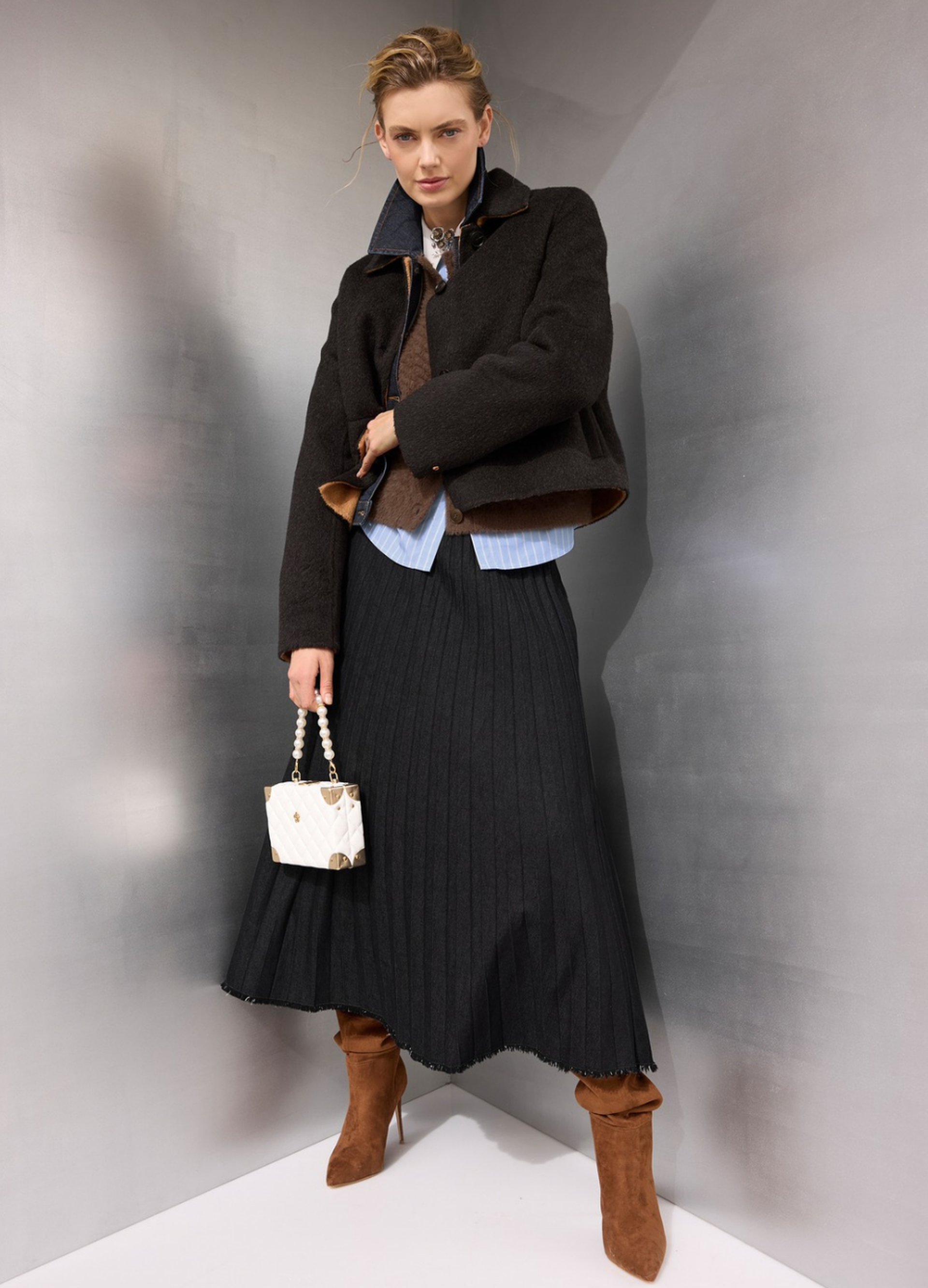 Moderner Zwiebellook mit kurzer dunkler Jacke, Bluse, langem Plisseerock und braunen Stiefeln
