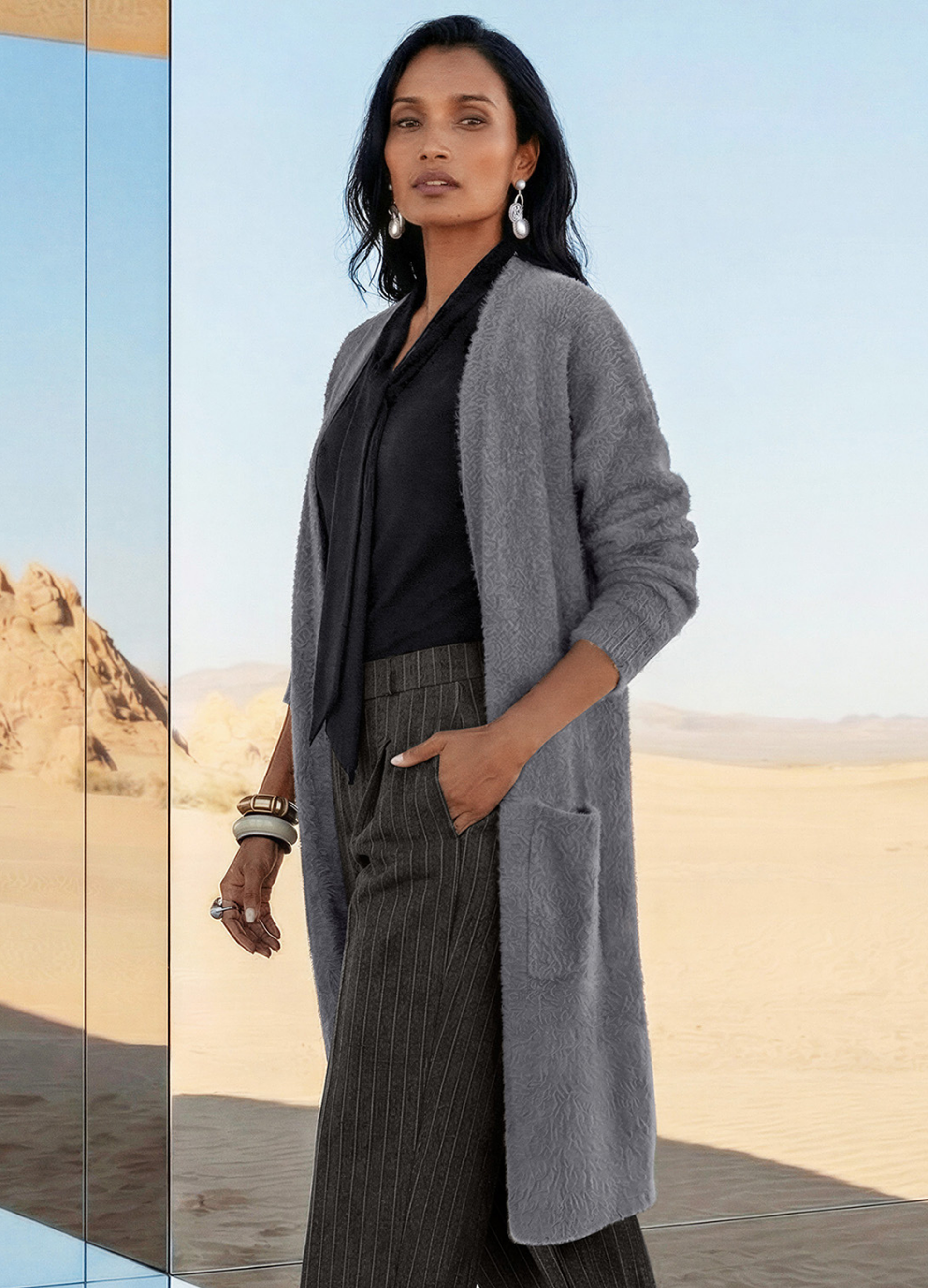 Frau im Layering-Look mit langem grauem Cardigan, schwarzer Bluse und Nadelstreifenhose