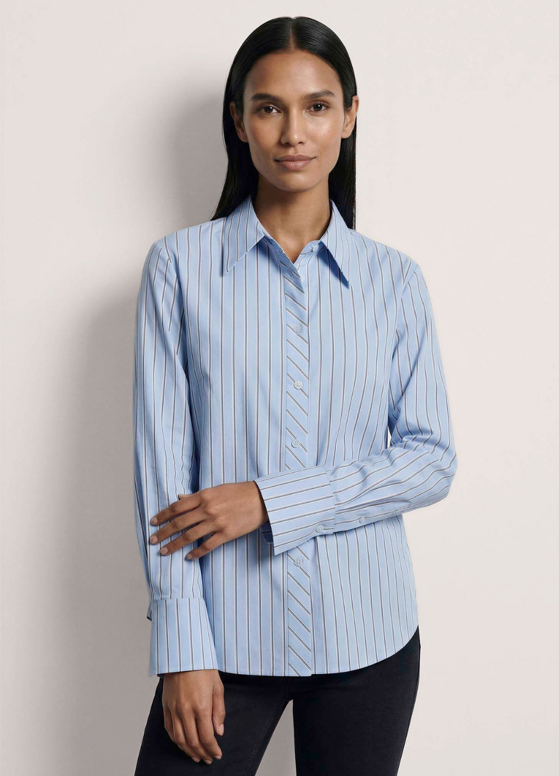 Frau in hellblauer Hemdbluse mit feinem Streifenmuster, langen Ärmeln und schwarzer Hose
