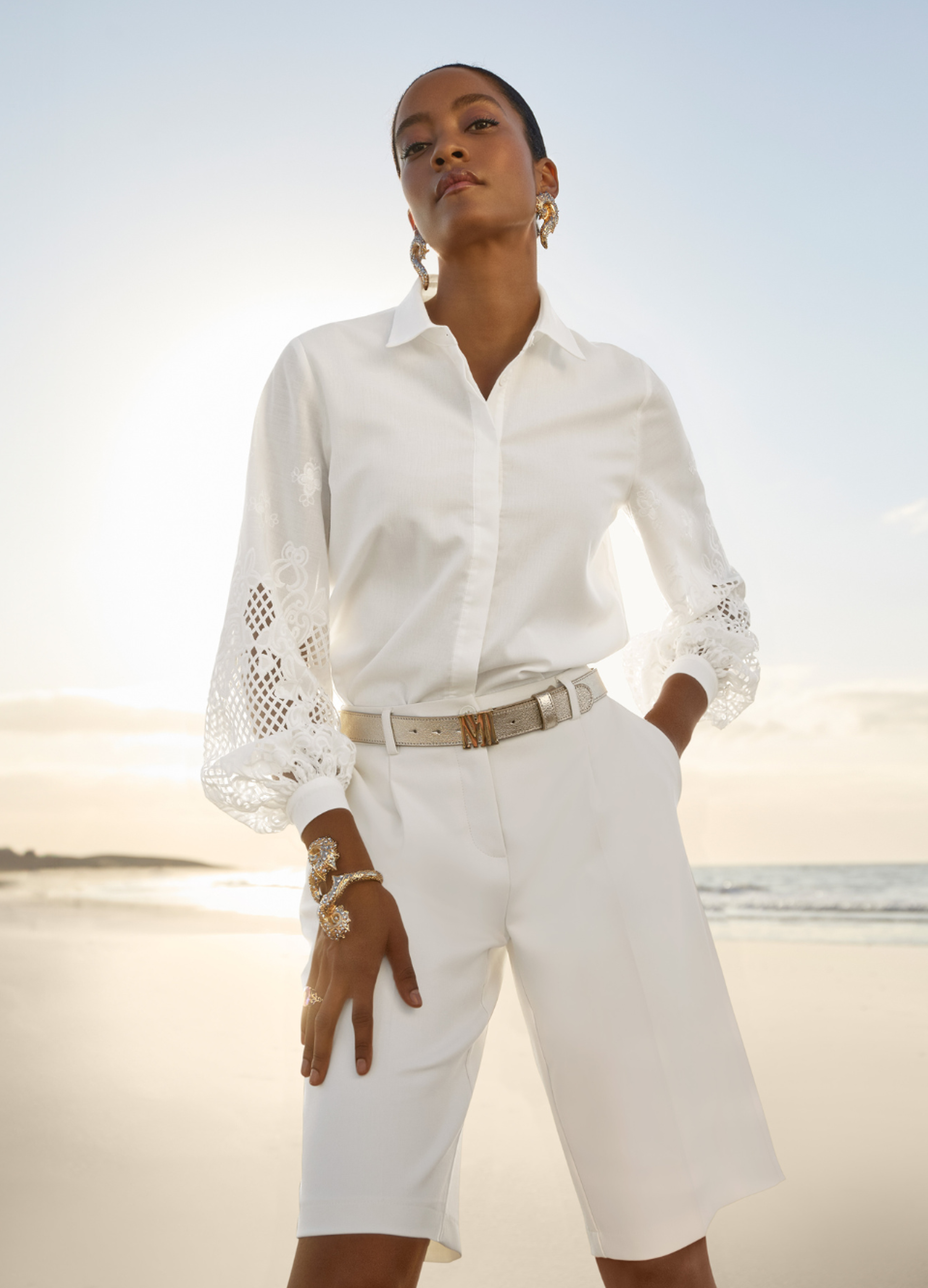 Eine Frau trägt eine Bluse in der Pantone® Trendfarbe „Cloud Dancer”. Sie kombiniert sie mit einer leichten Kurzhose in derselben Farbe. Als Accessoire wurde ein silberner Gürtel von MADELEINE gewählt.