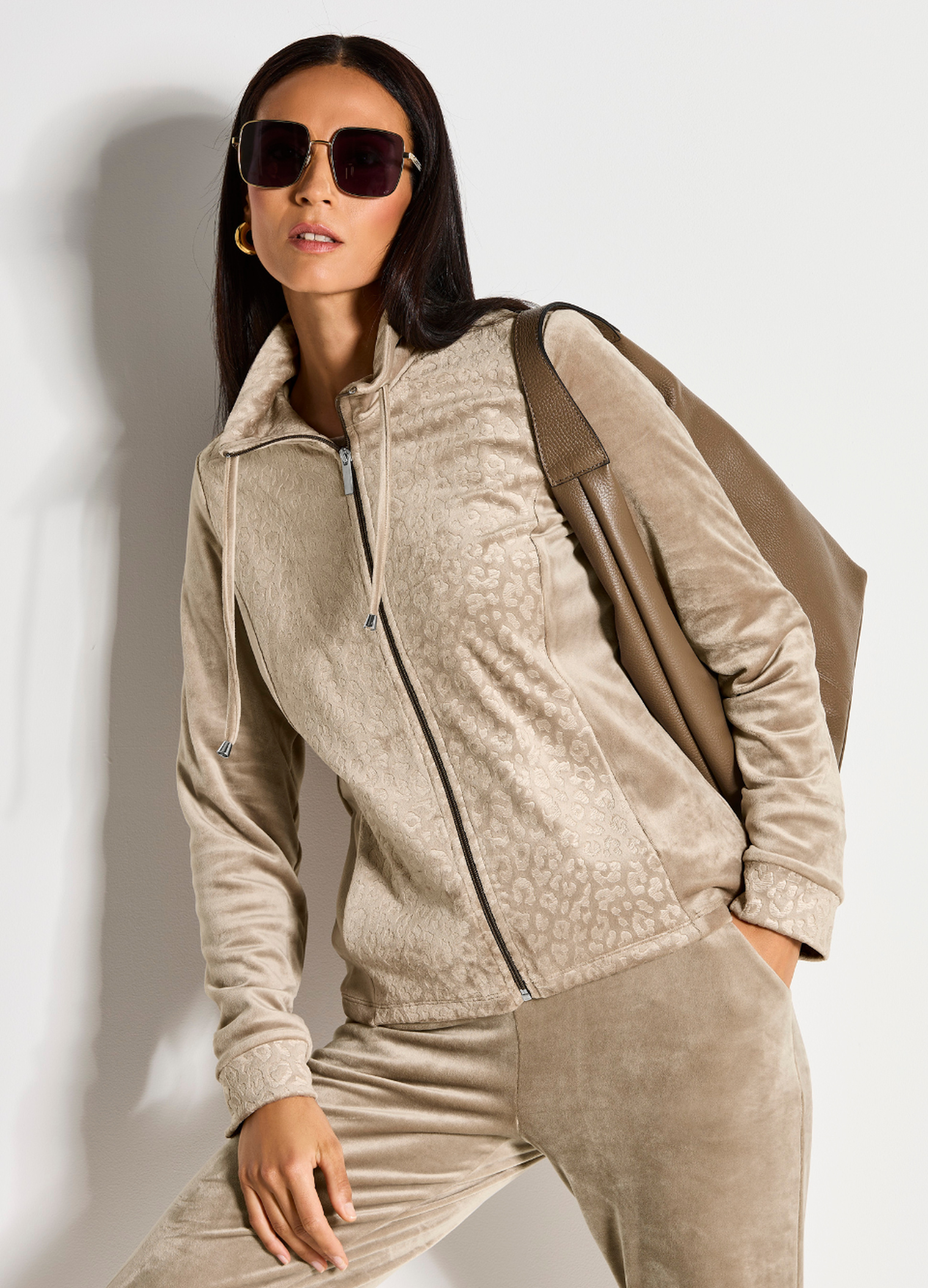 Eine Frau trägt einen gemütlichen Hausanzug, dazu kombiniert sie eine Sonnenbrille und eine Handtasche.