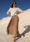 Dame in weißem Strick-Pullover und Caramel-farbenen Plissee-Rocknen 