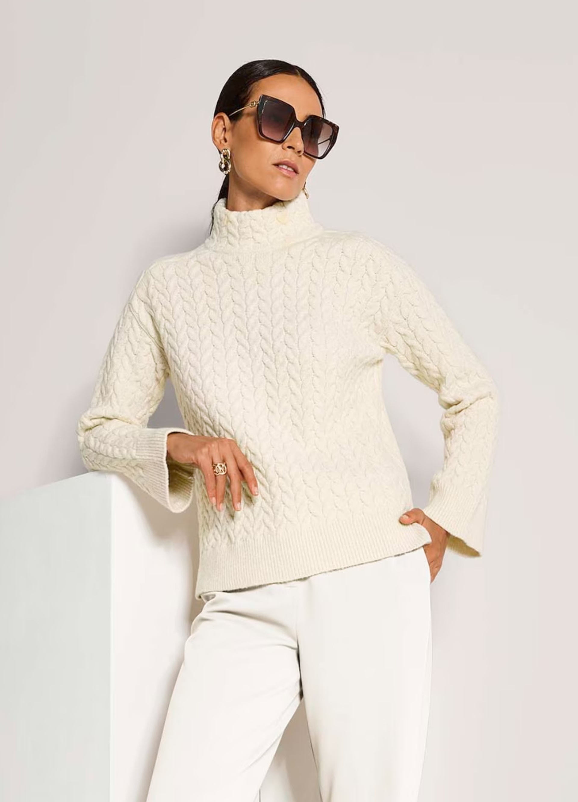 Eine Frau trägt einen beigen Stehkragenpullover im Strick-Look. Er wirkt schlicht, kuschelig und elegant.