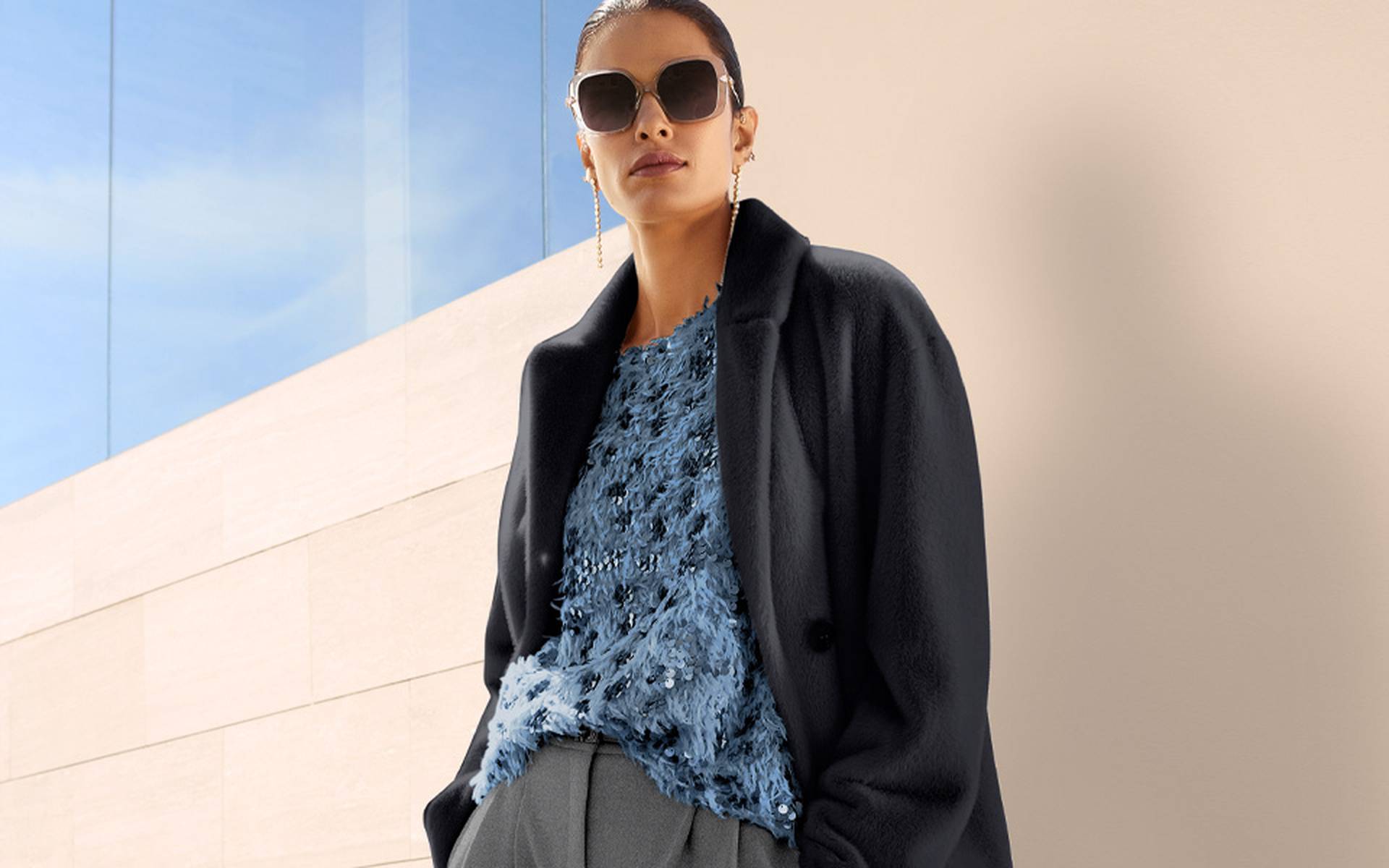 Blue knit top with a round neckline and textured surface, embellished with sequins and glitter details, worn under a dark blazer.