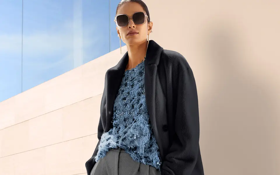 Haut en maille bleu avec encolure ronde et surface texturée, orné de sequins et de détails scintillants, porté sous un blazer foncé.