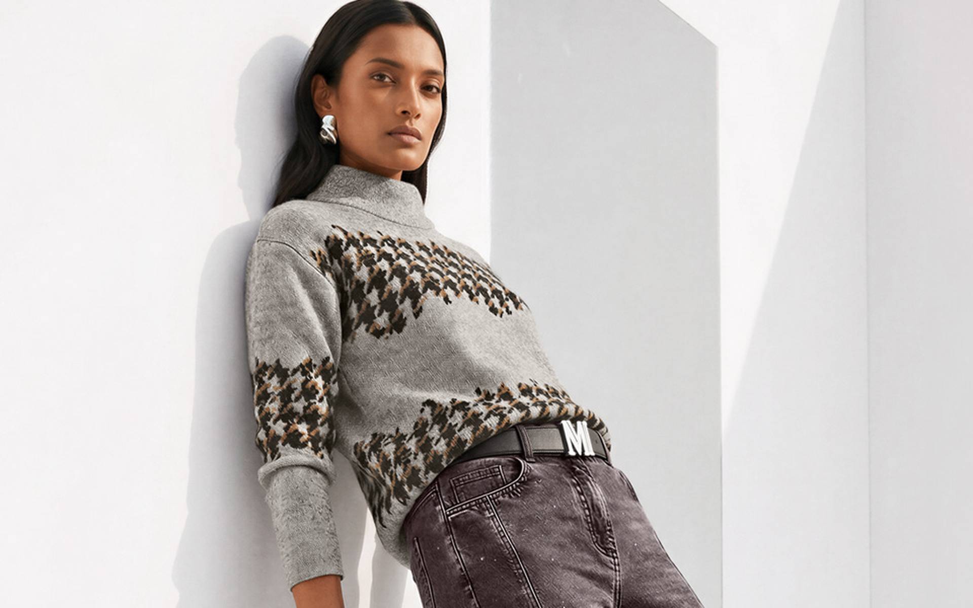 Light grey knit sweater with a stand-up collar and brown and black jacquard pattern, casually paired with trousers.