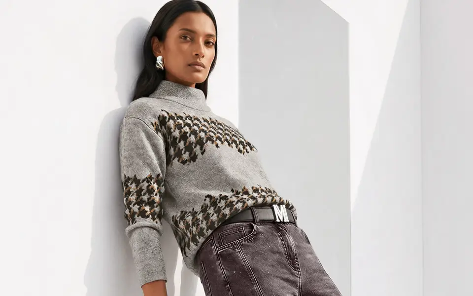 Pull en maille gris clair à col montant, motif jacquard brun et noir, associé de façon décontractée à un pantalon.