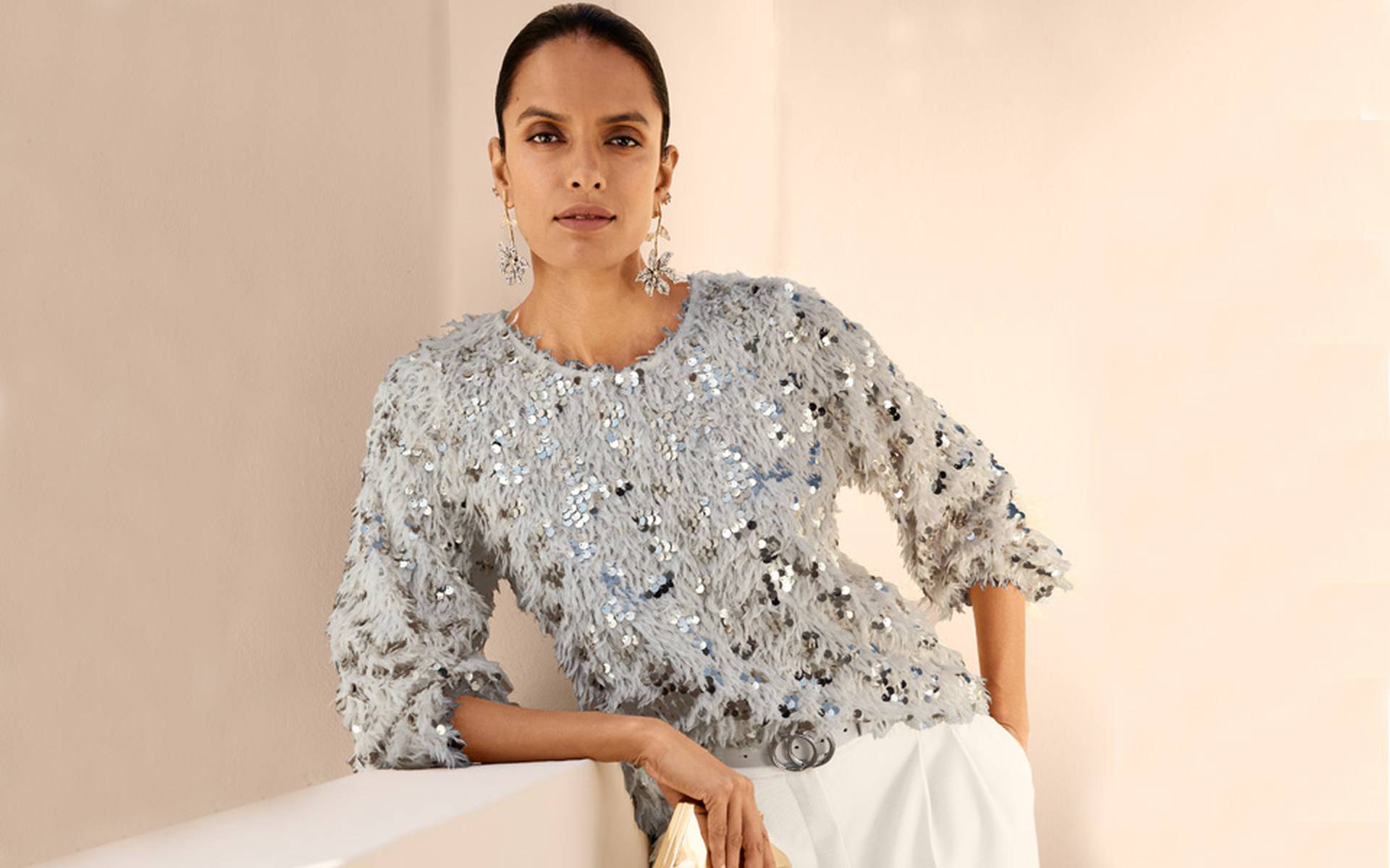 Light grey knit top with a round neckline, three-quarter sleeves and trim featuring sequins, rhinestones and a fringed texture.