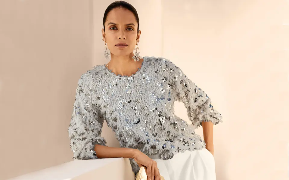 Haut en maille gris clair avec encolure ronde, manches trois-quarts et finitions en sequins, strass et texture à franges.