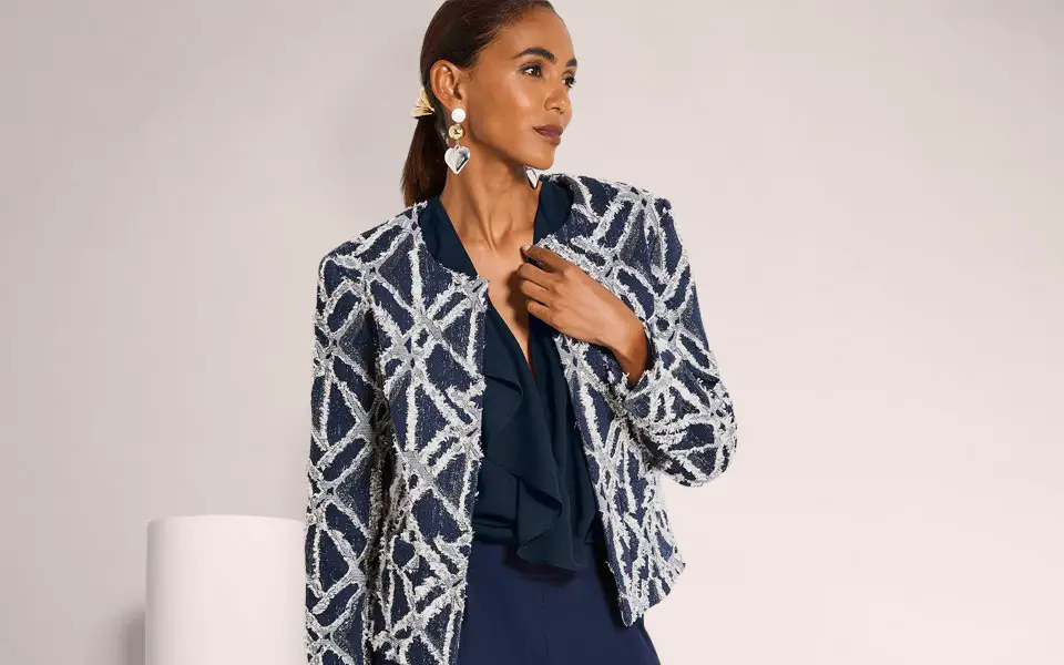 Blazer court bleu marine à motif texturé graphique blanc, porté ouvert sur un chemisier à détail volanté.