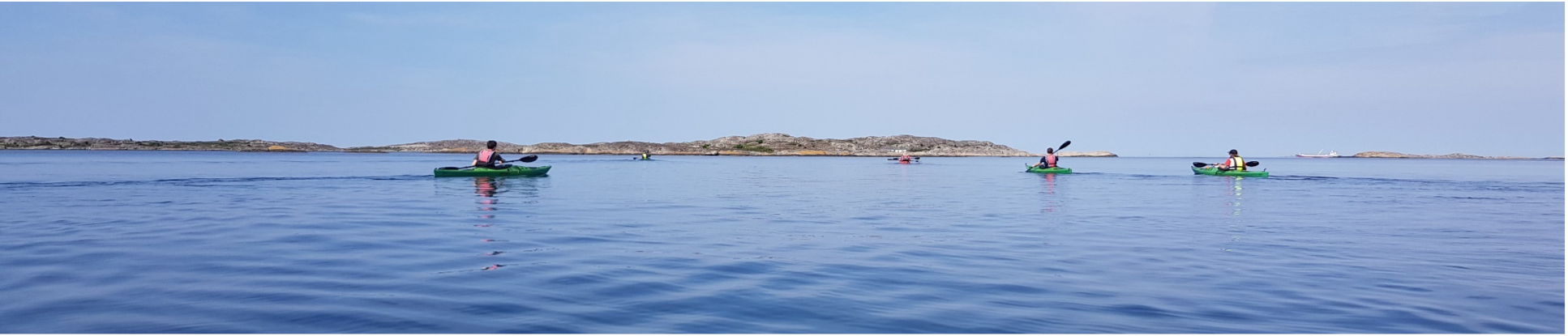 People kayaking on calm blue water, with rocky islands in the background under a clear sky.