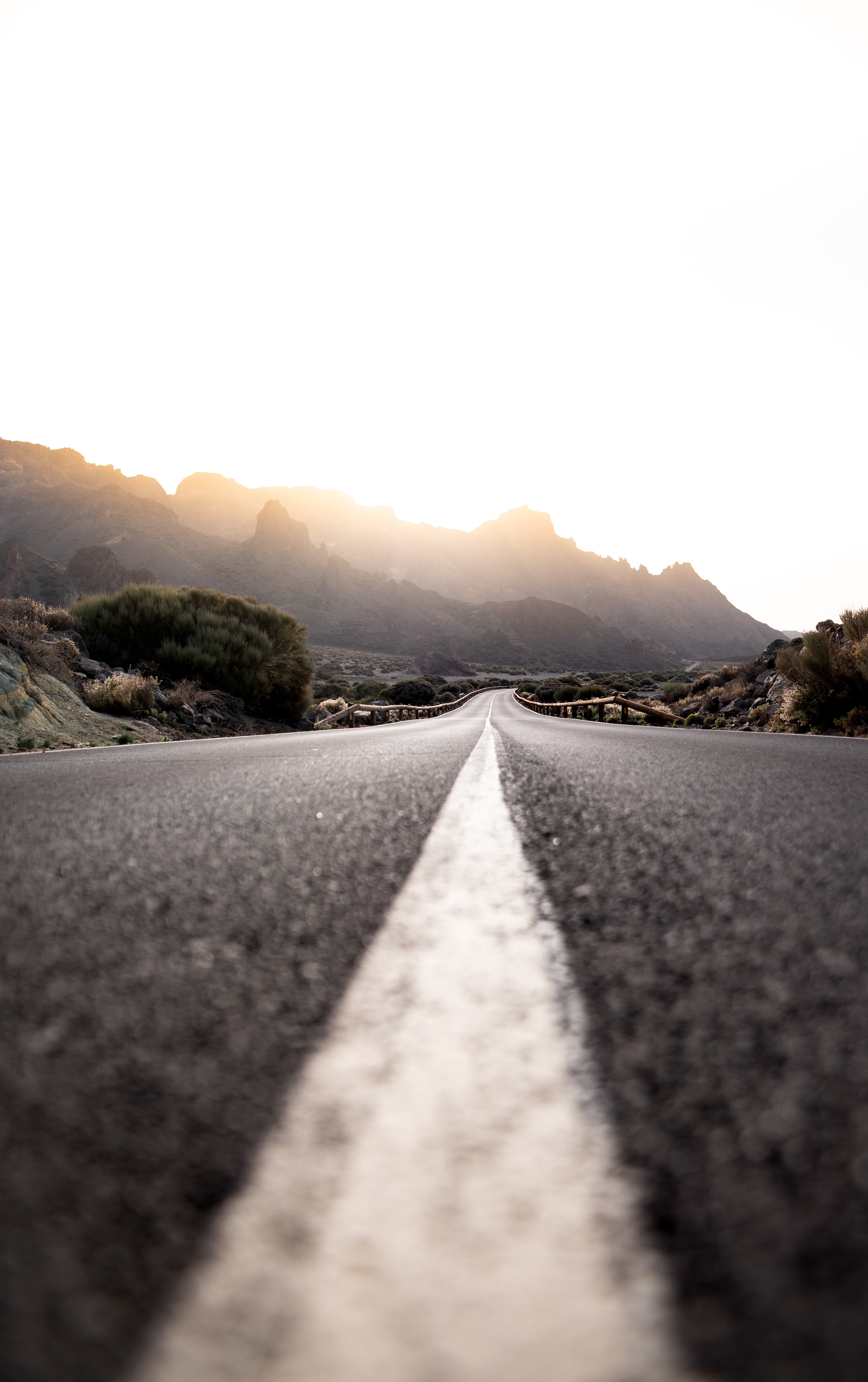 Camino vacío con línea blanca en el medio y montañas al fondo durante la puesta de sol.