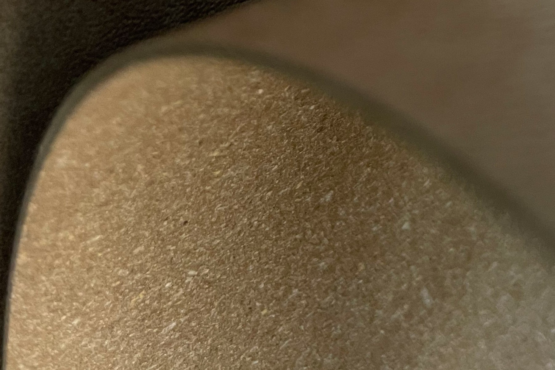 Close-up view of a beige, textured surface, possibly a fabric or material, with a slightly blurred background.