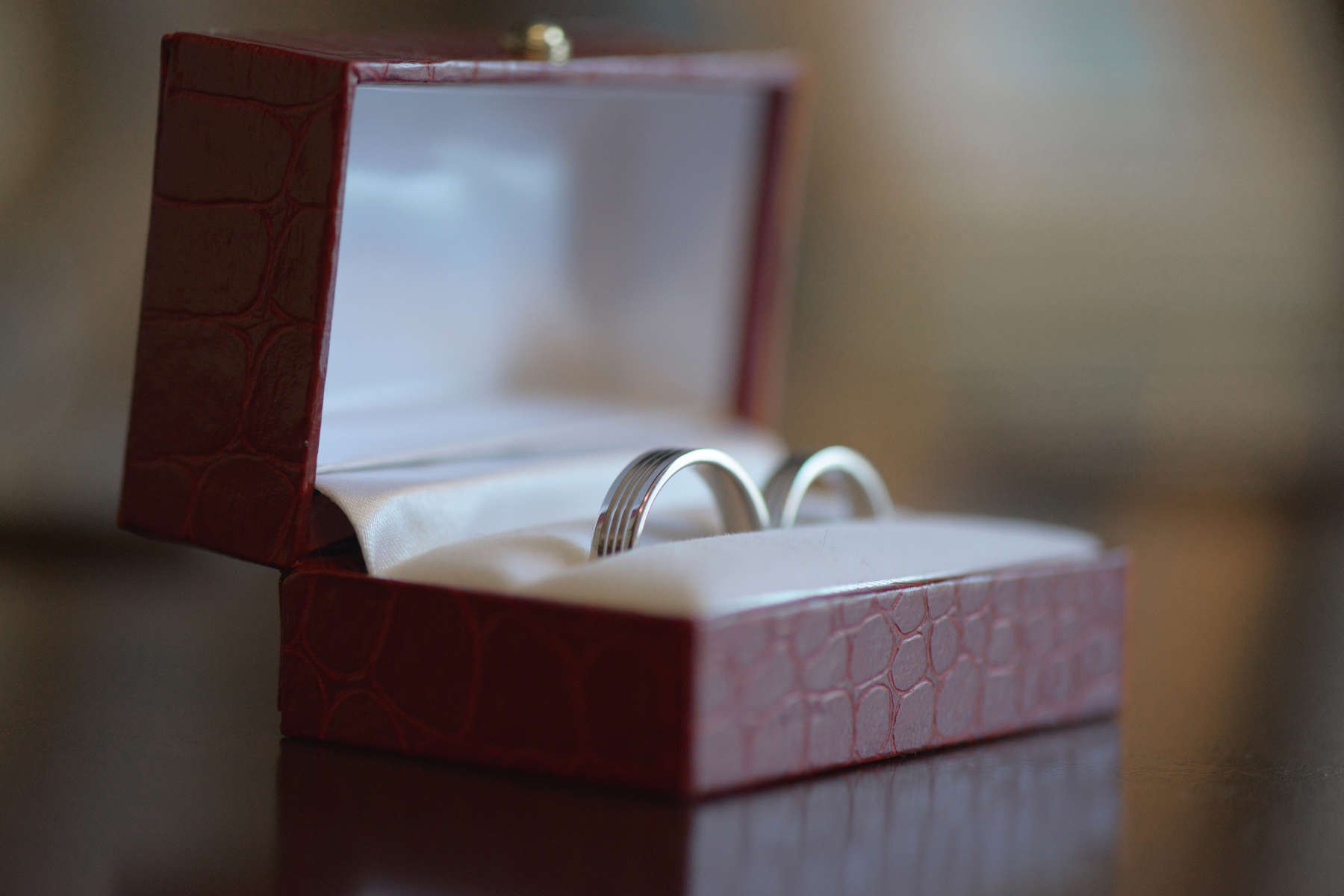 Two silver wedding rings in a red leather box with a white satin lining, placed on a wooden surface.