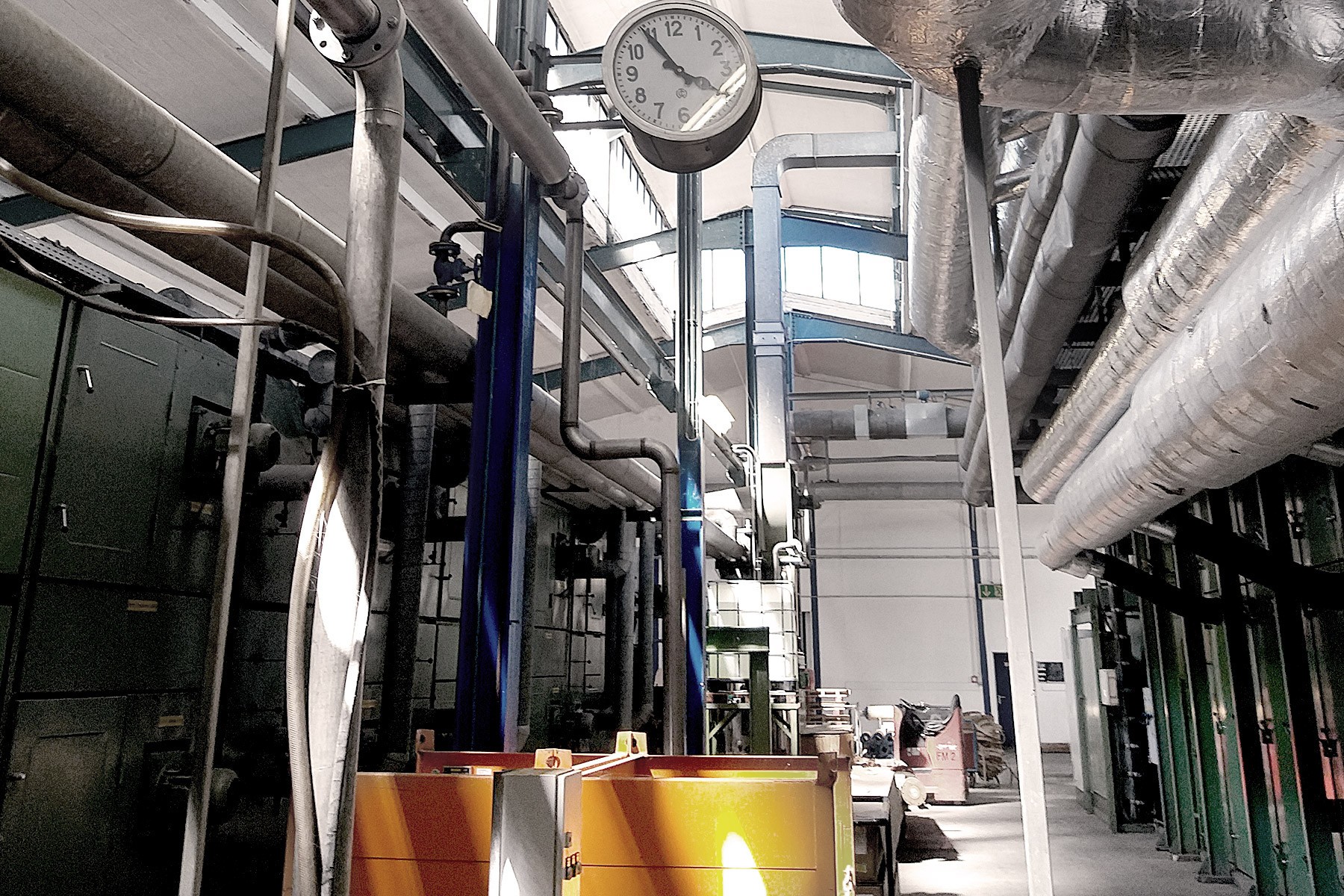 Eine große Industrieanlage mit Rohren, Maschinen und einer Uhr, die von der Decke hängt und die Zeit 10:10 anzeigt.